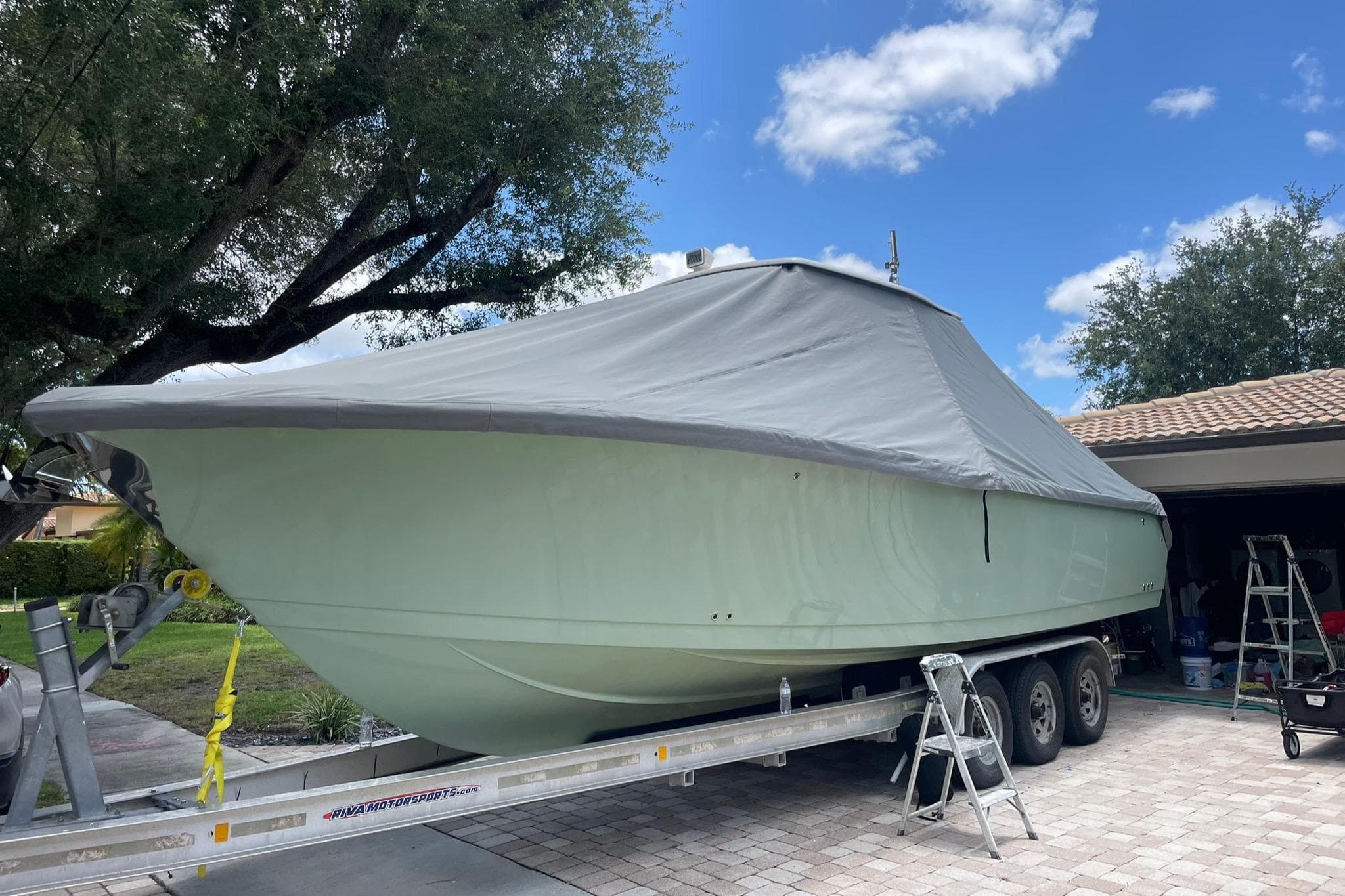 2014 Sailfish 320 CC boat on trailer, covered, parked in driveway under blue sky.
