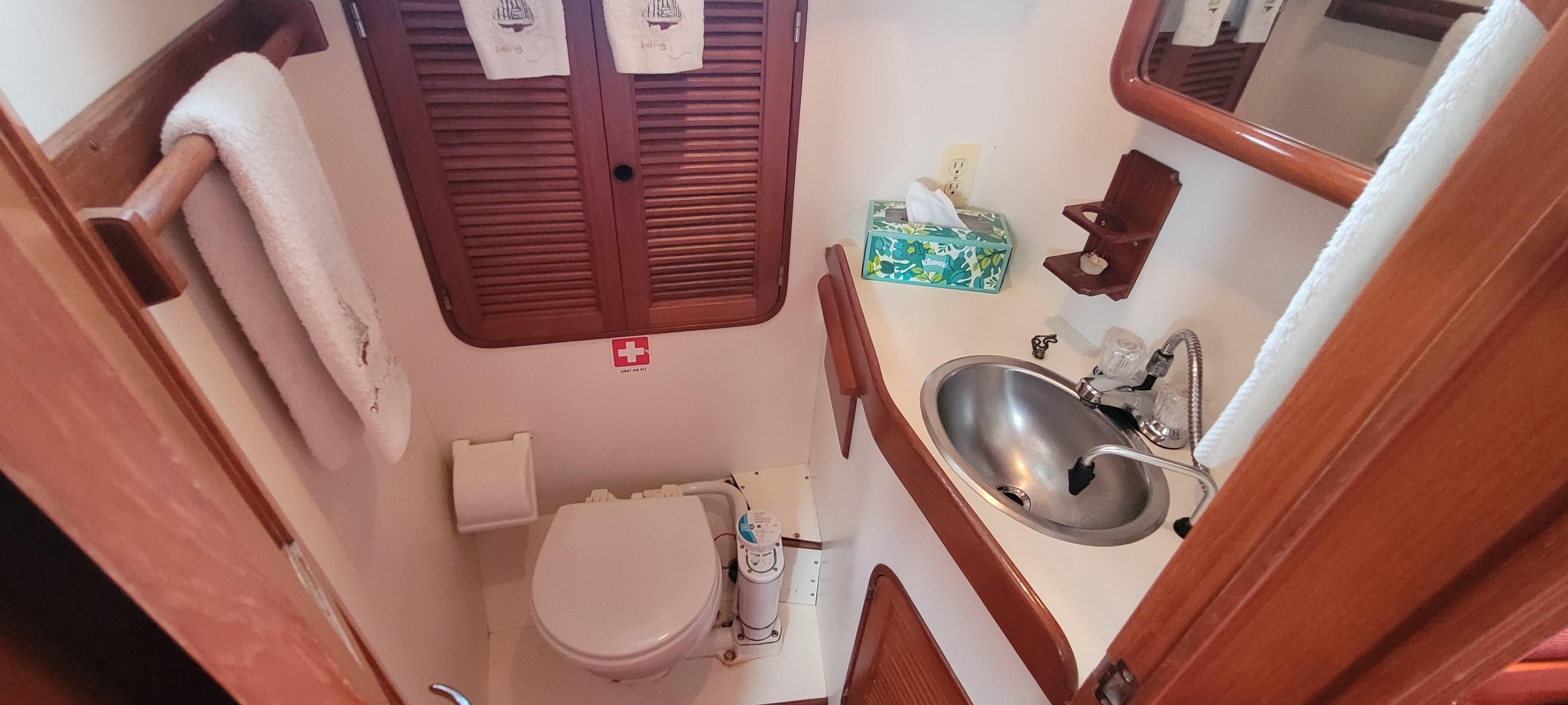 Compact bathroom in a 1985 Mason 33 Sloop, featuring a sink, toilet, and wooden cabinetry.