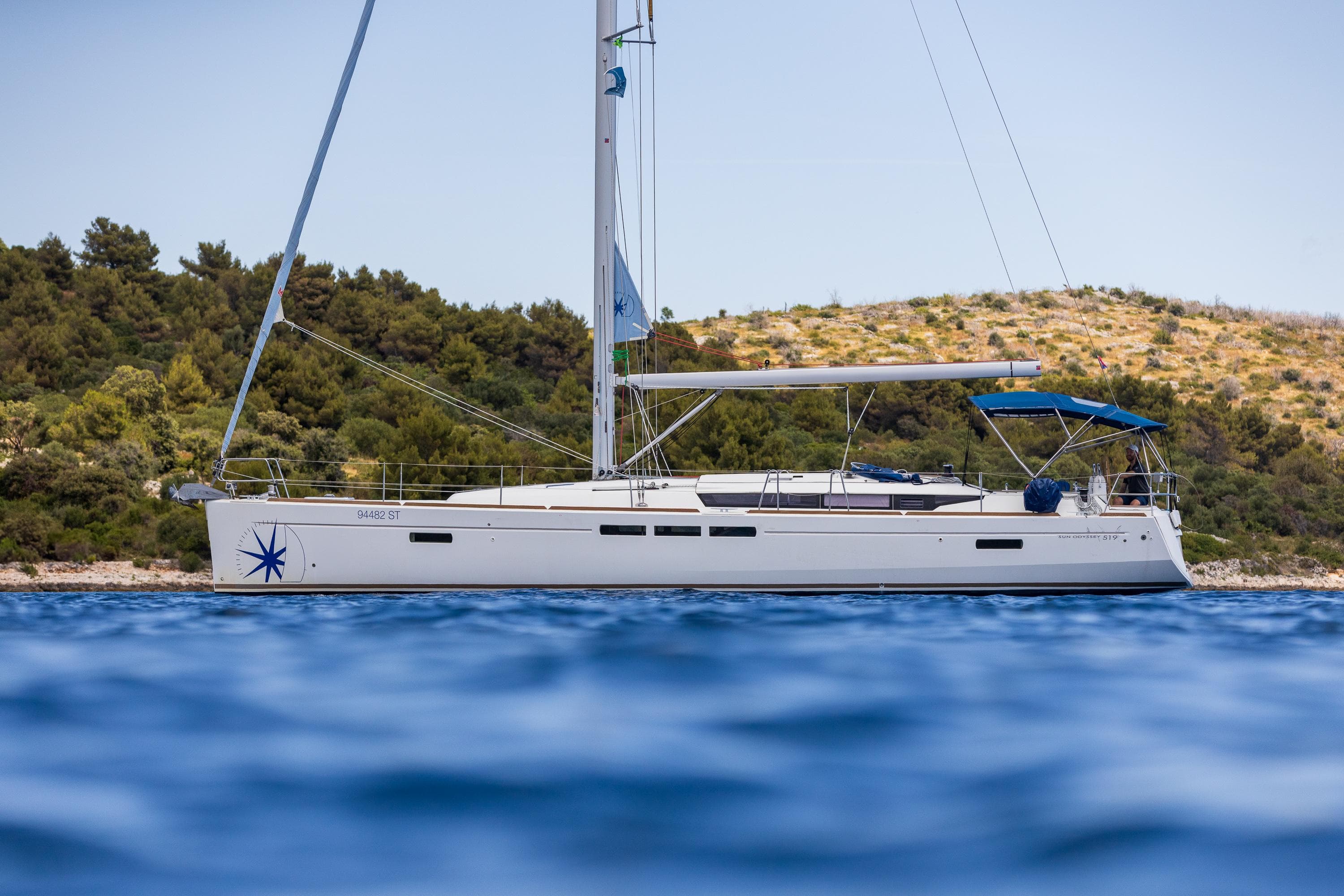 2018 Jeanneau Sun Odyssey 519 sailing yacht on calm waters near a scenic coastline.