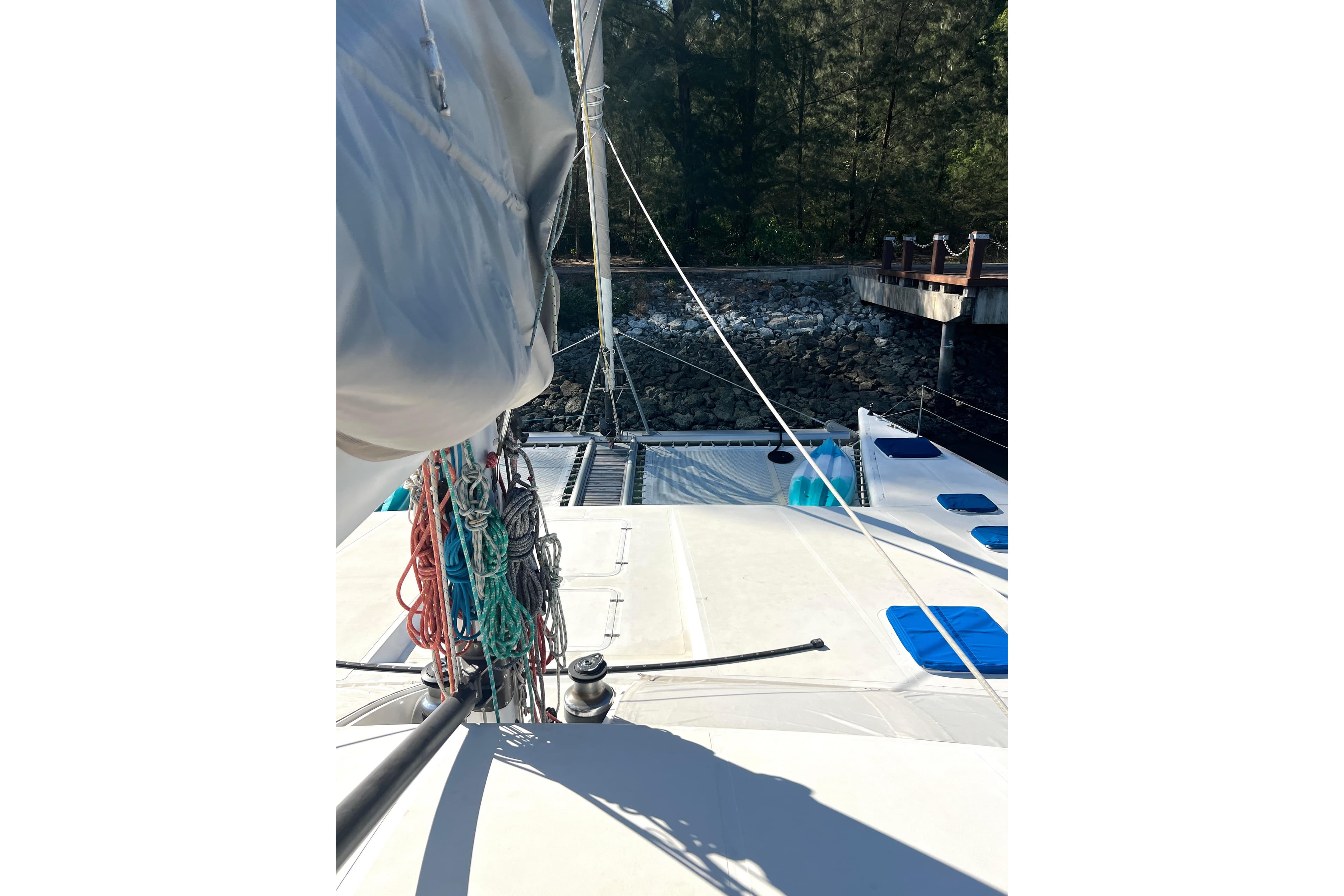 Catamaran deck view with ropes and sails, Concordia Dickson 69, 2005 model, docked near rocky shore.
