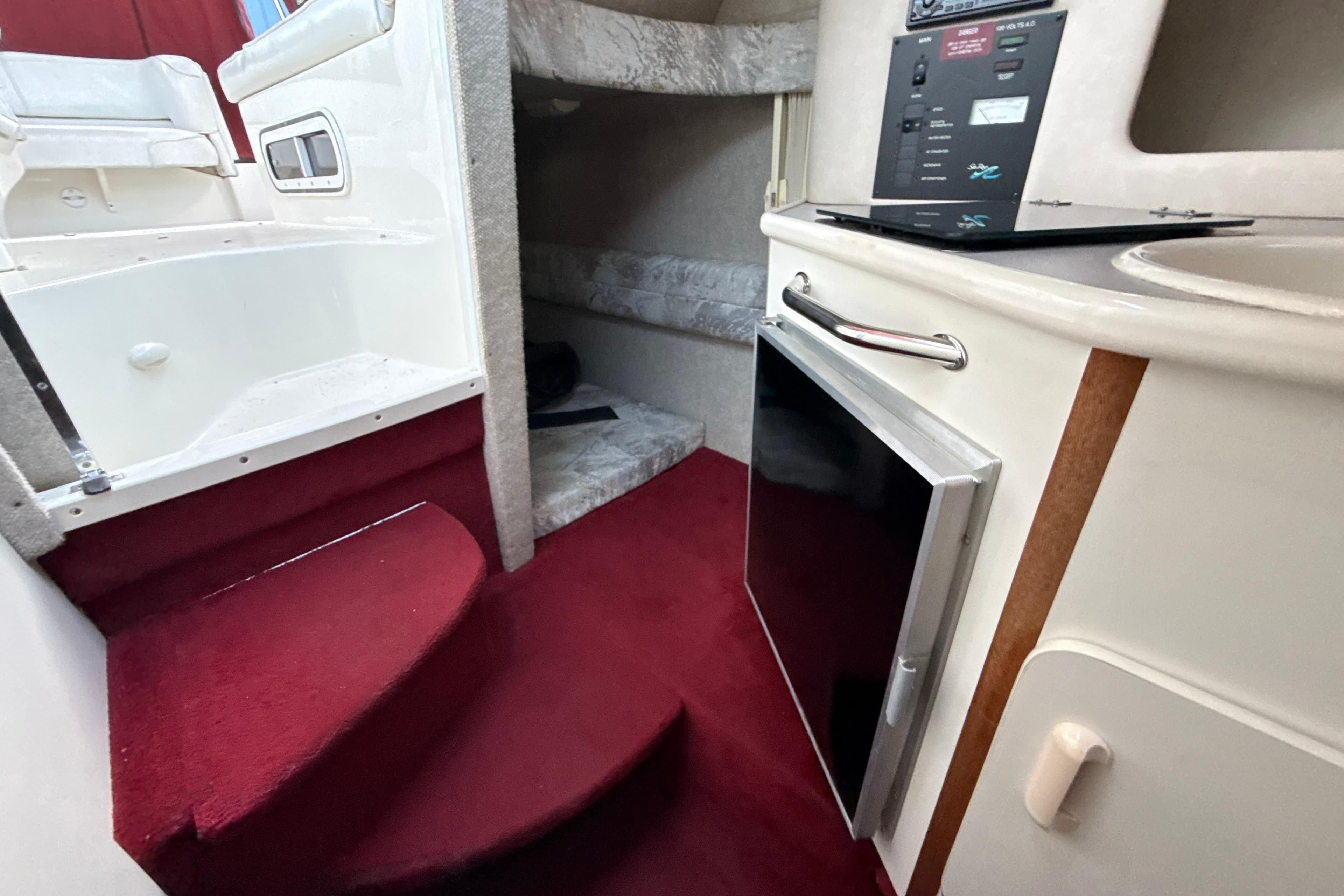 Interior of a 1996 Sea Ray 240 Sundancer boat with red carpet and compact kitchenette.