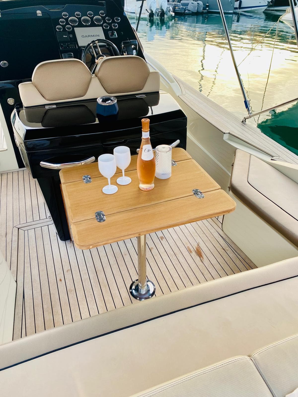 Luxury yacht deck with wooden table, wine bottle, and glasses; serene marina backdrop.