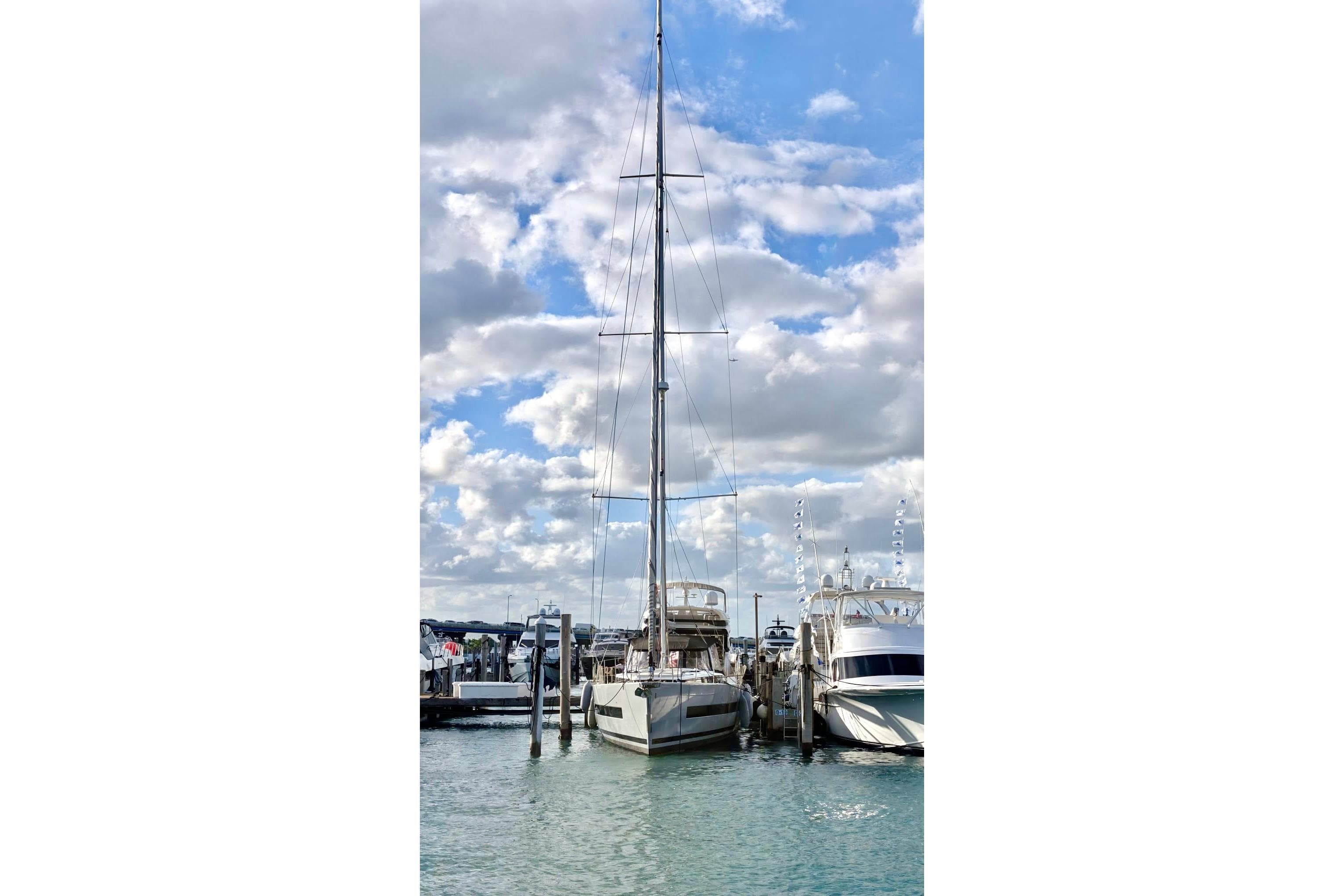 2019 Beneteau Oceanis Yacht 62 docked at marina under cloudy sky.