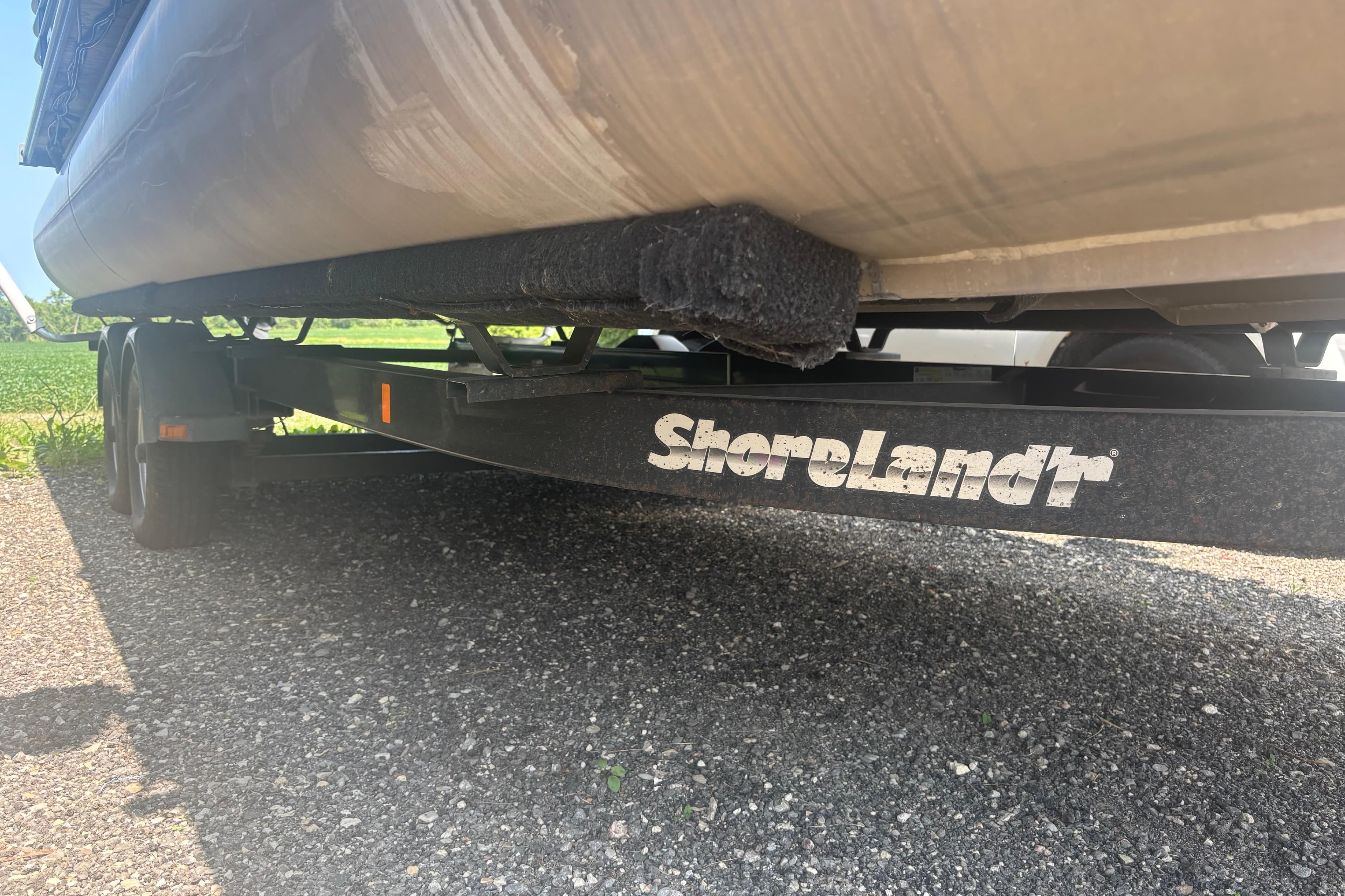 Trailer with 2016 Legend 25 boat on ShoreLand'r trailer, parked on gravel.