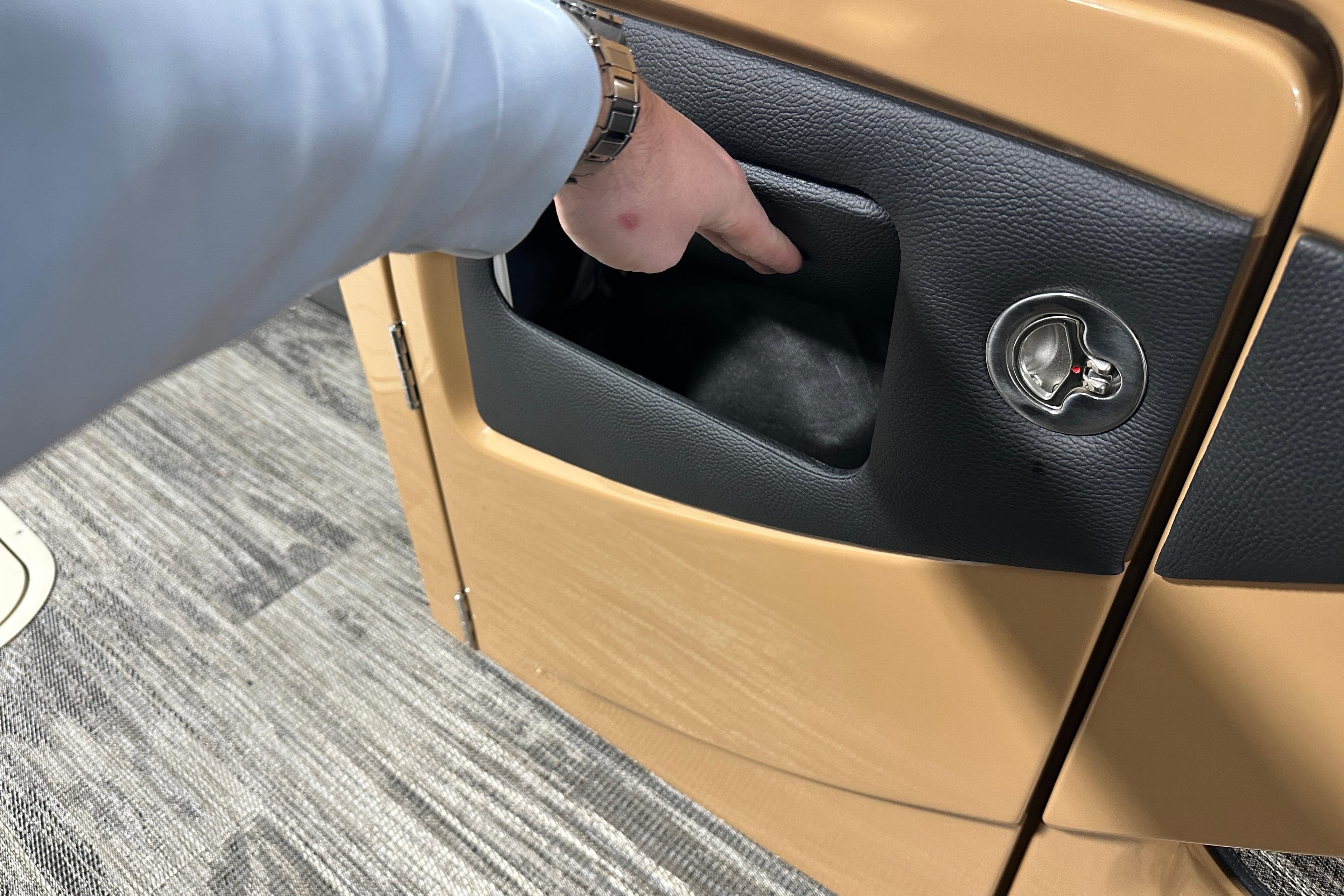 Hand accessing storage compartment in 2026 Godfrey Monaco 255 SB boat interior.