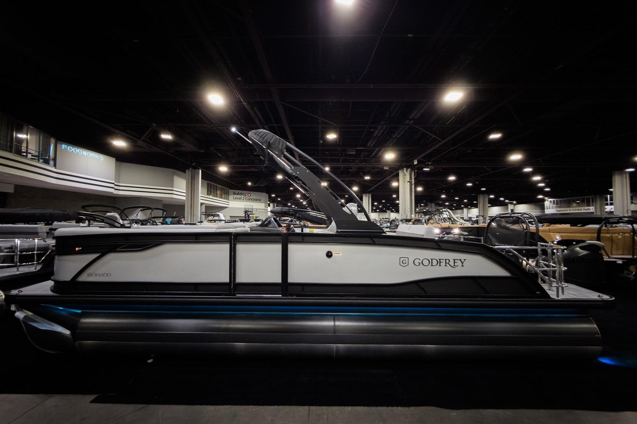 2026 Godfrey Monaco 25' Tritoon boat displayed indoors, showcasing sleek design and modern features.