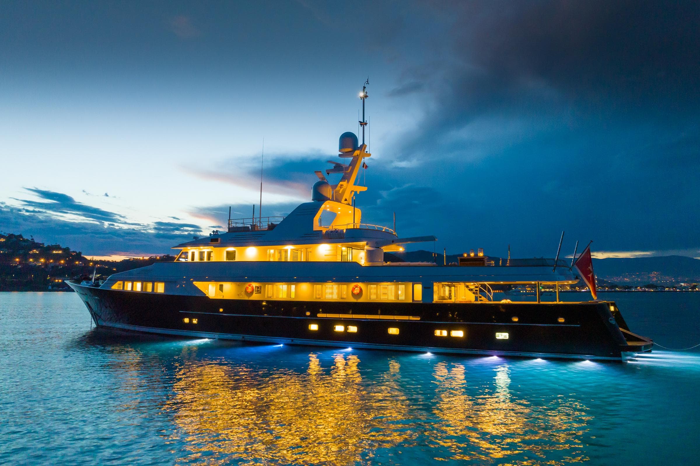 Luxurious 1990 Feadship yacht illuminated at dusk on calm waters.
