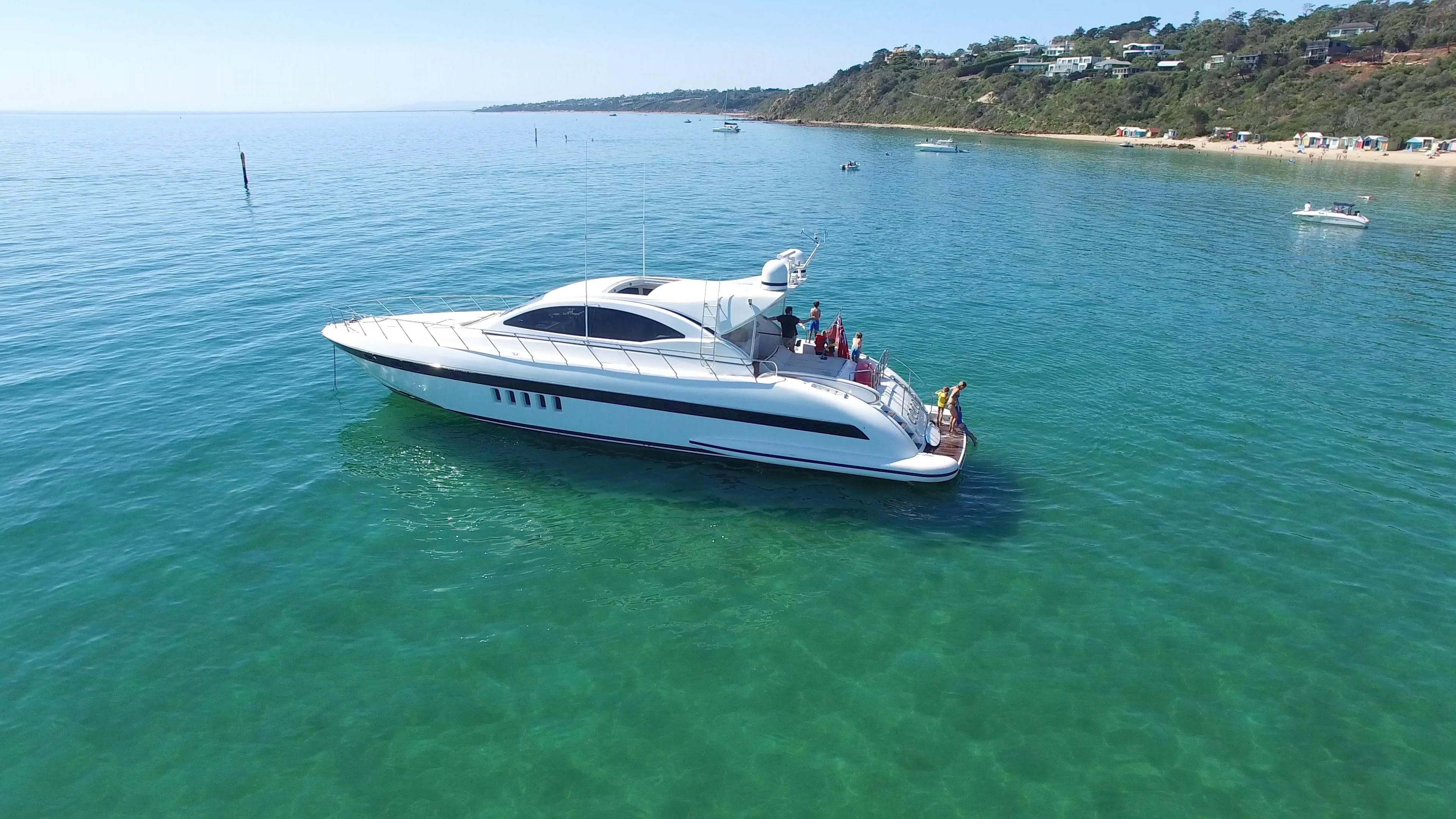 Luxury 2002 Mangusta 72 yacht cruising on clear blue waters near a scenic coastline.