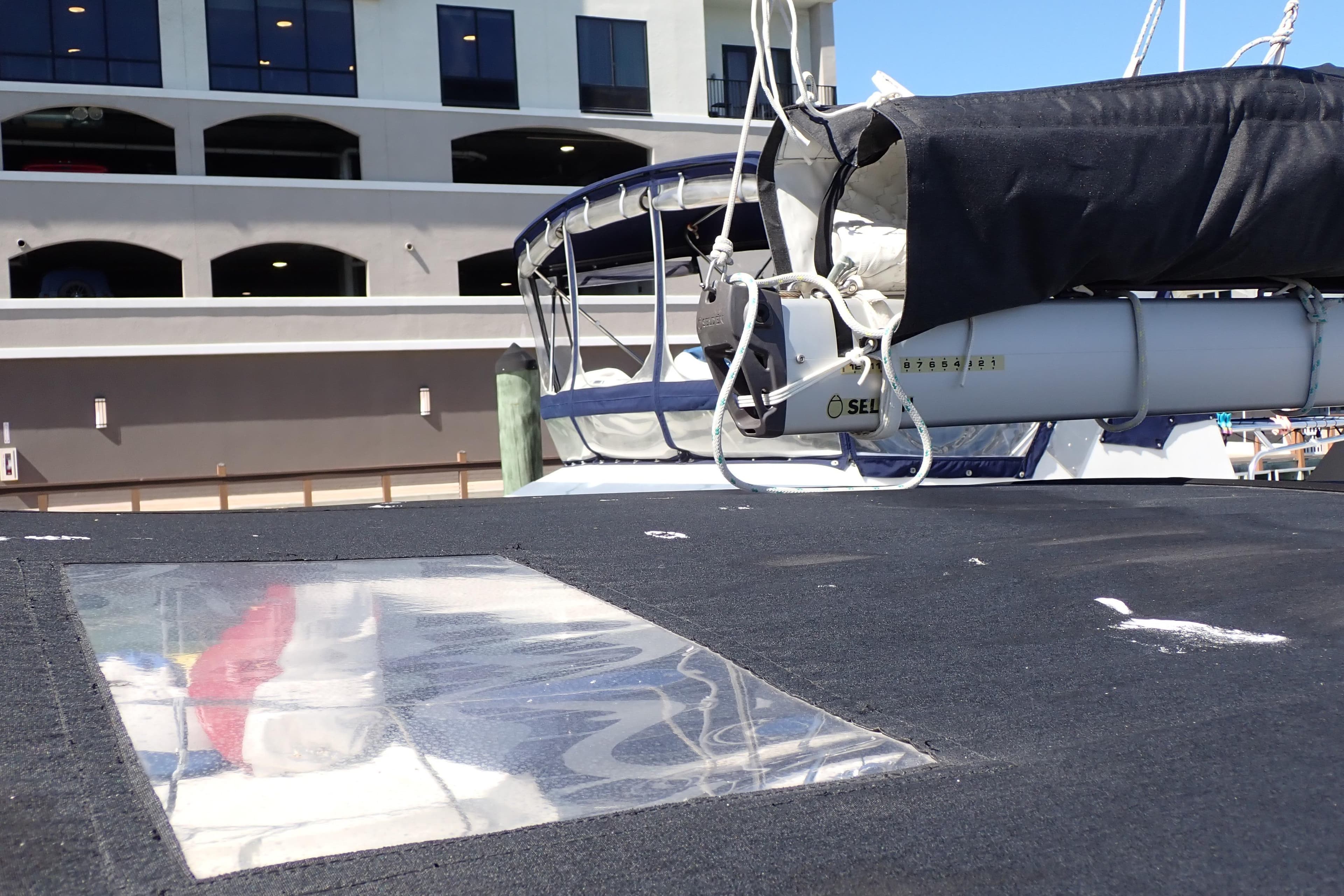 2018 Jeanneau Sun Odyssey 389 sailboat deck with covered boom, docked near a building.