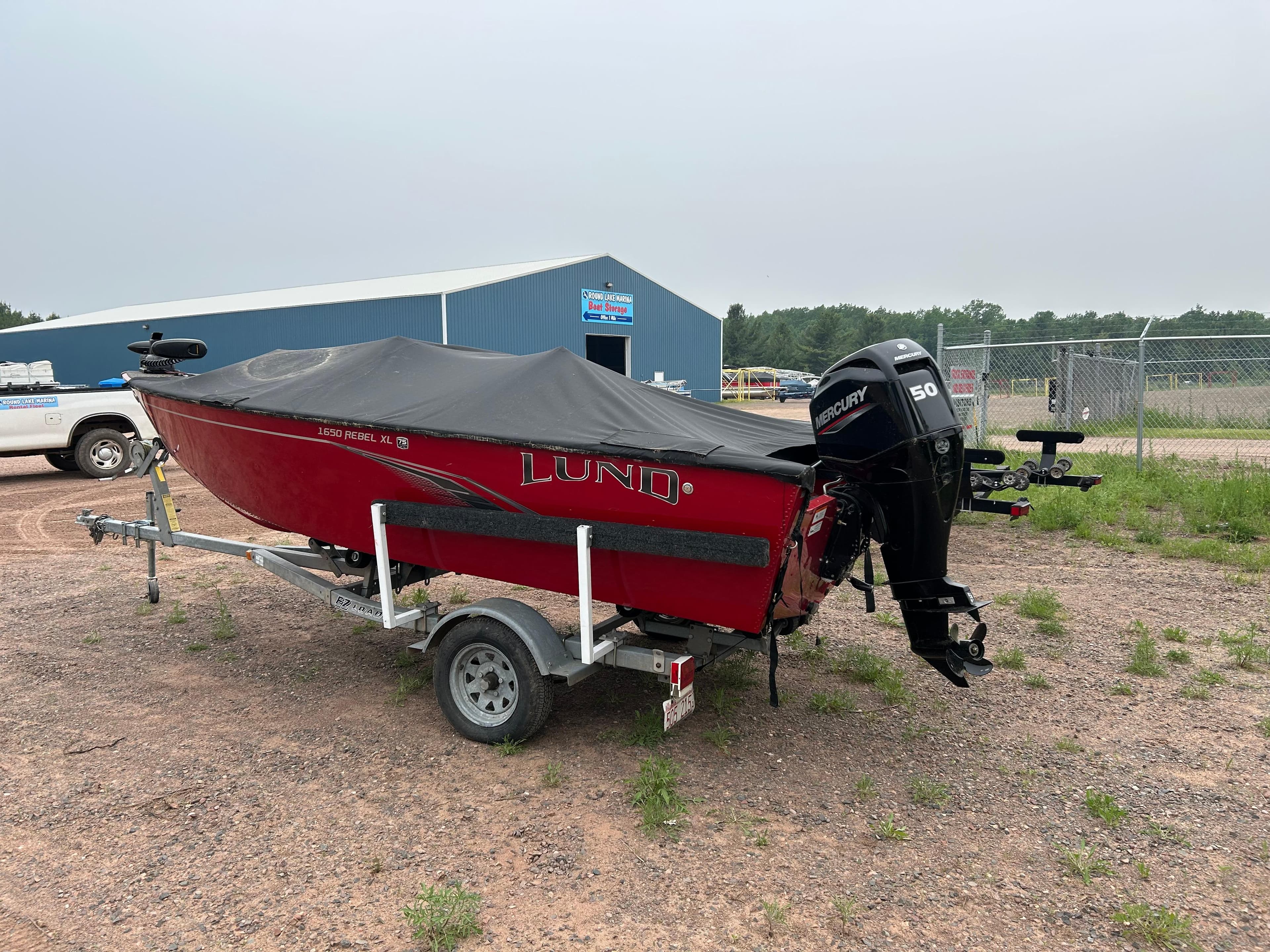 2023 Lund 1650 Rebel XL Sport boat on trailer with cover, parked outdoors.
