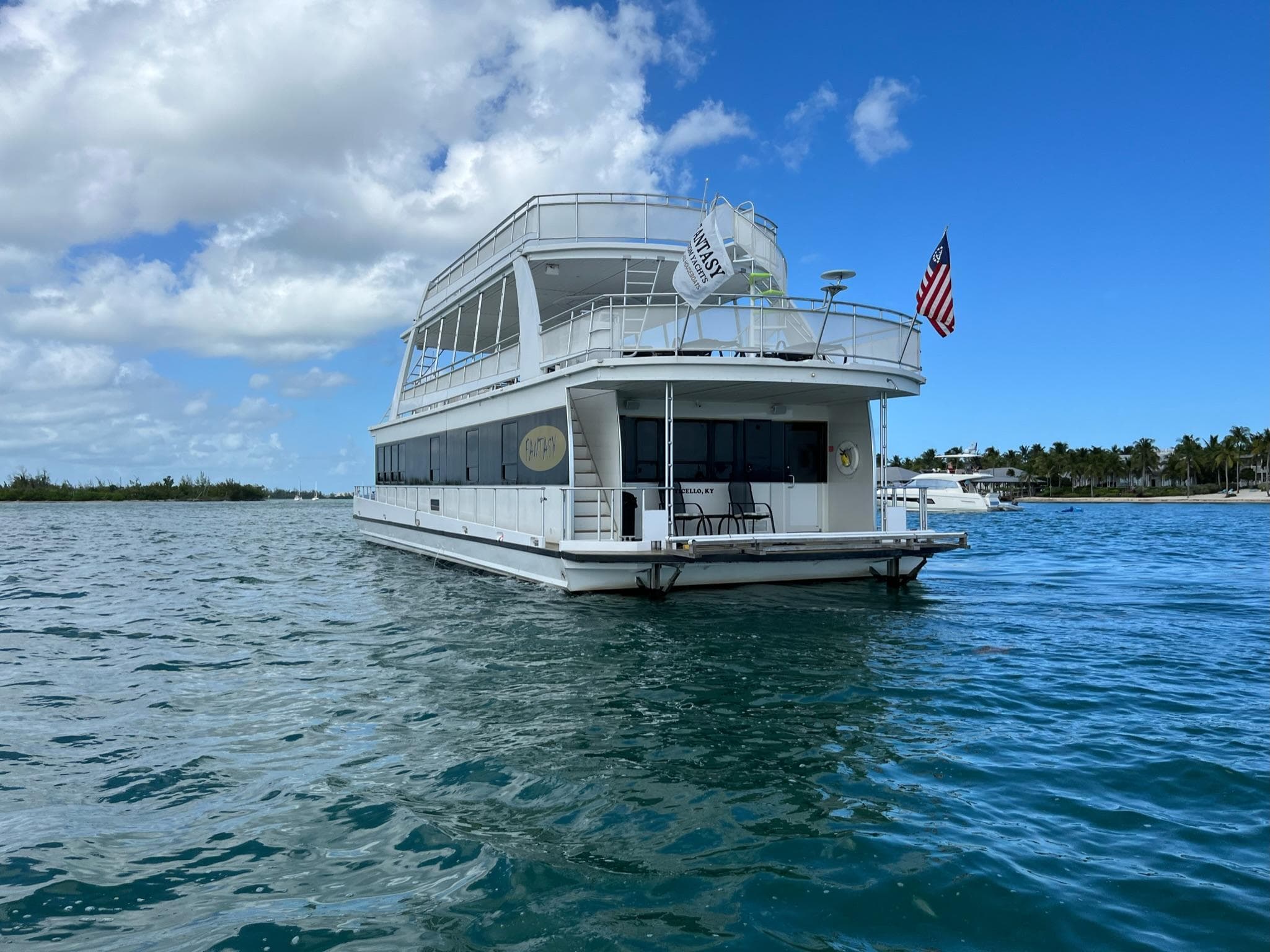 White 2009 Fantasy Houseboat on calm blue water under a partly cloudy sky.