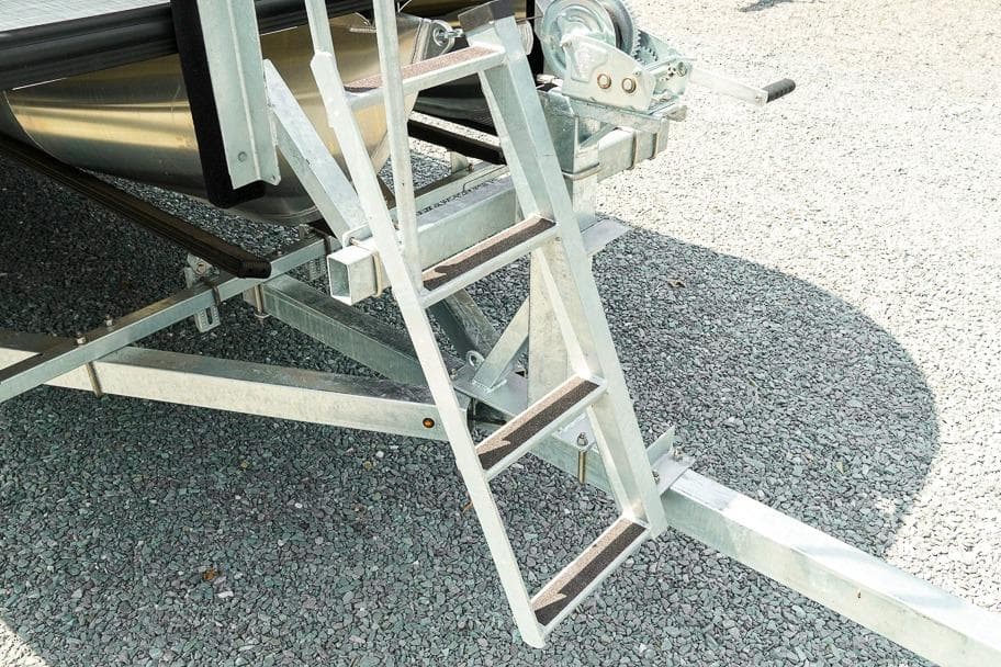Aluminum ladder on Dockside Pontoons 22DQ trailer, 2026 model, on gravel surface.