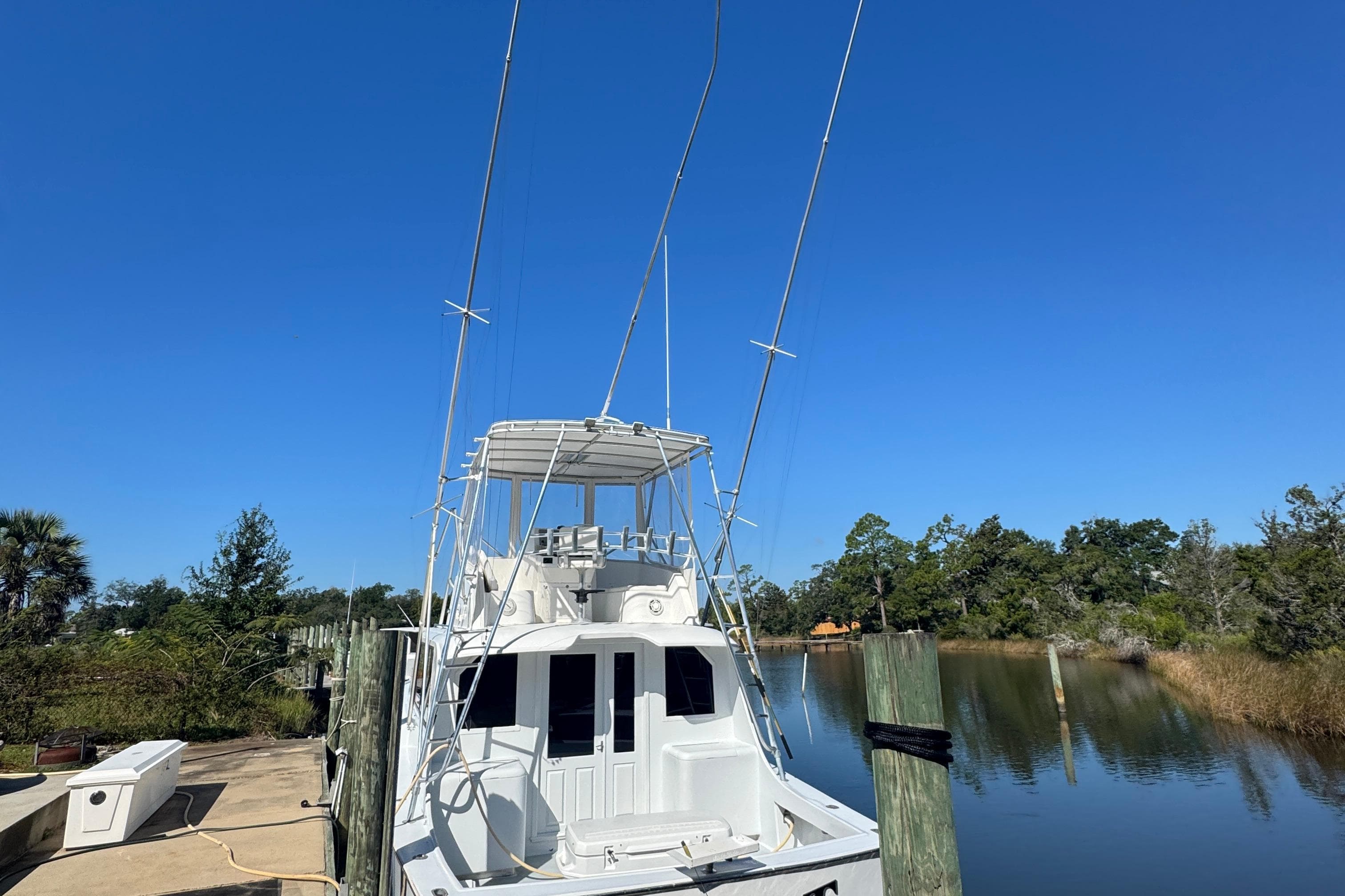 1965 Hatteras 41 Convertible boat docked by a serene waterway, clear blue sky.