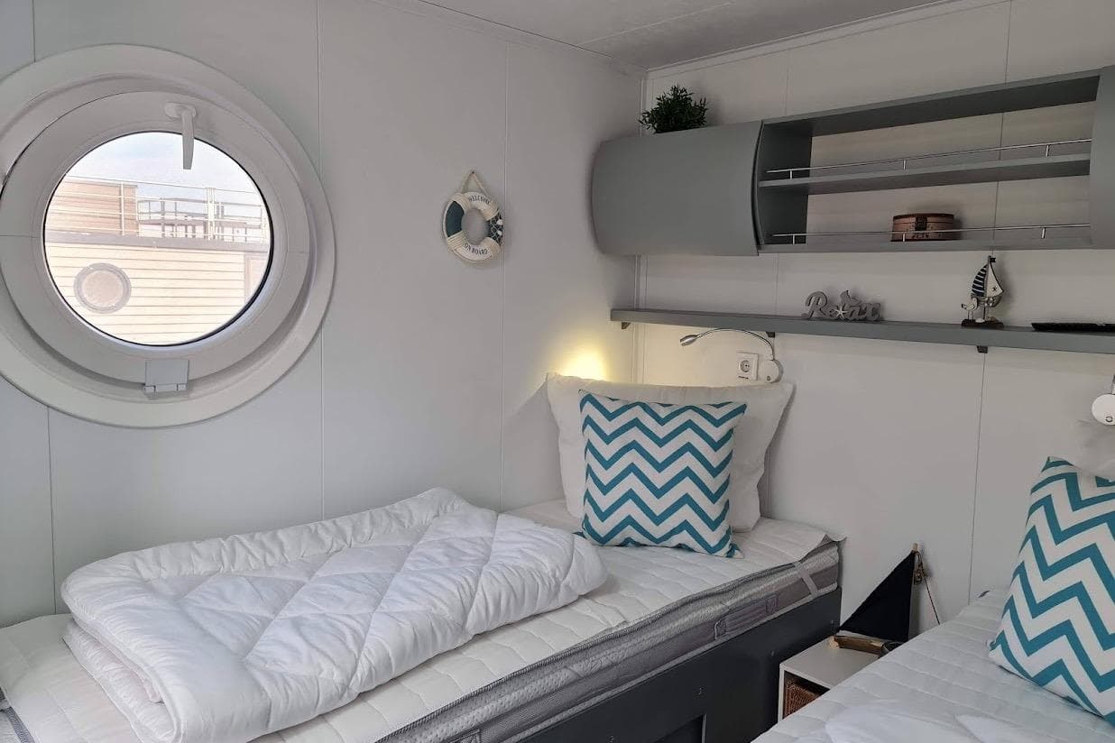 Cozy cabin interior with twin beds, nautical decor, and a porthole window on a 2022 Woma D13.