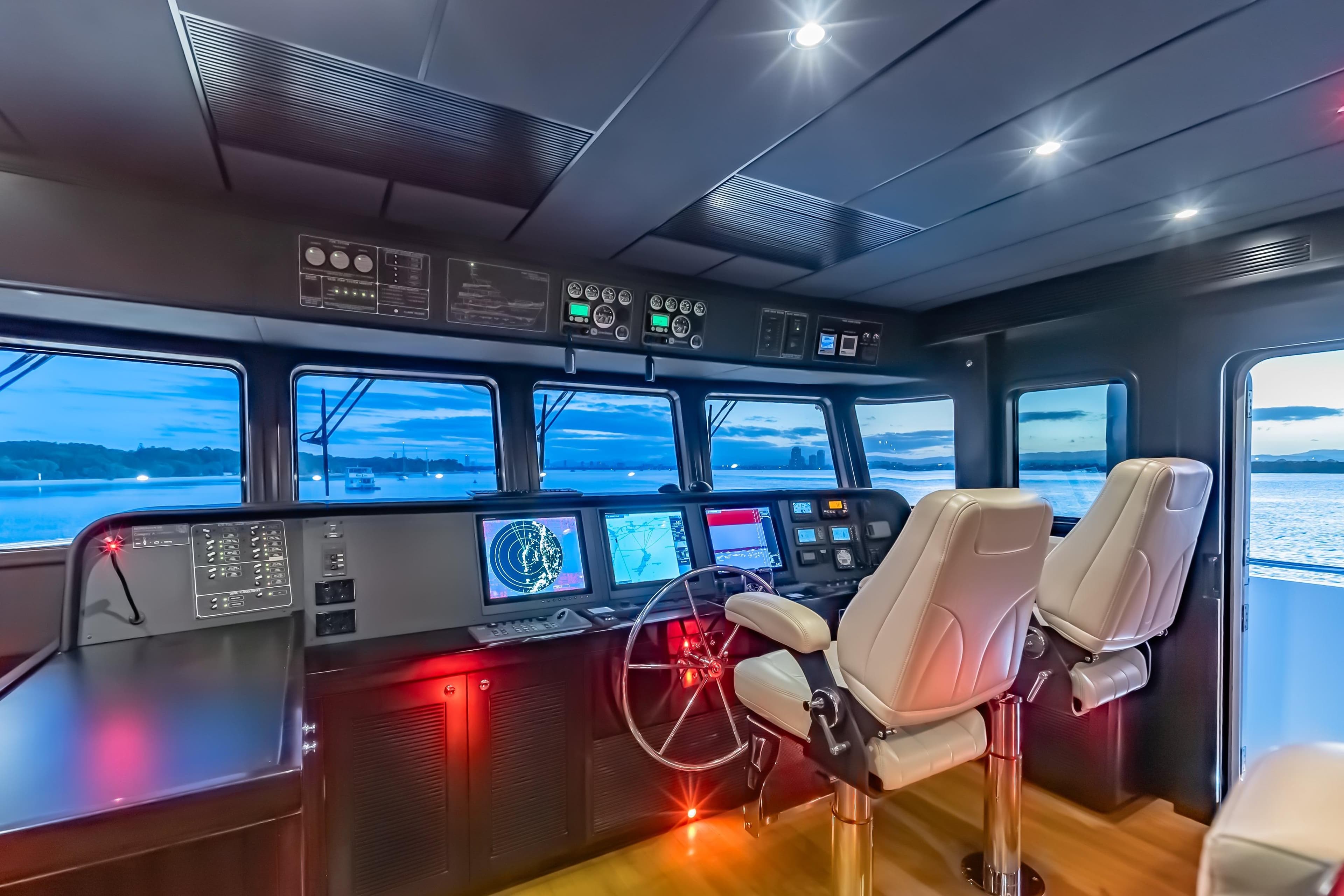 Pilothouse of 2013 Nordhavn 68 yacht with navigation equipment and panoramic windows at sunset.