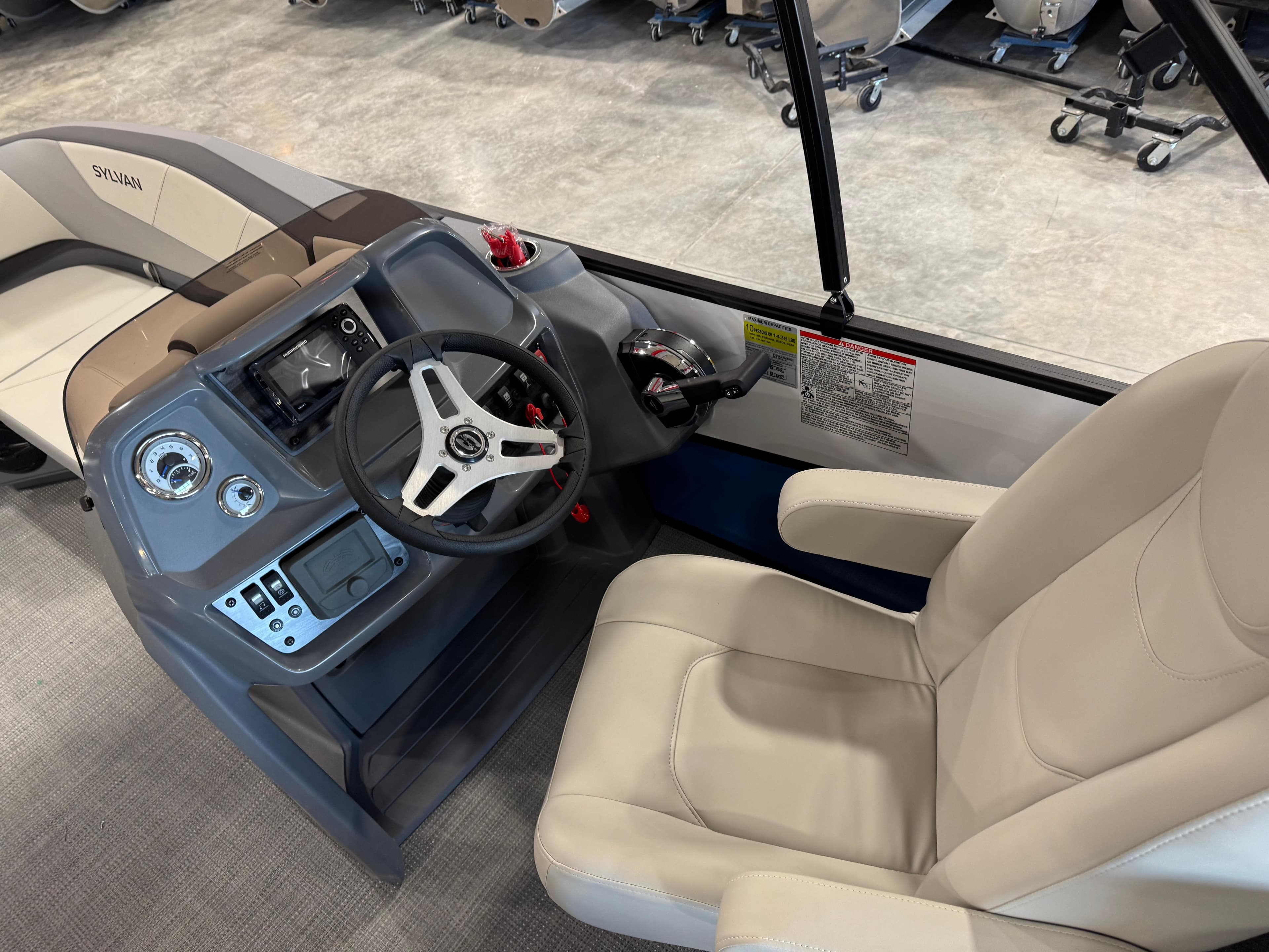 2025 Sylvan A-22 Sport boat interior with steering wheel and beige seating.
