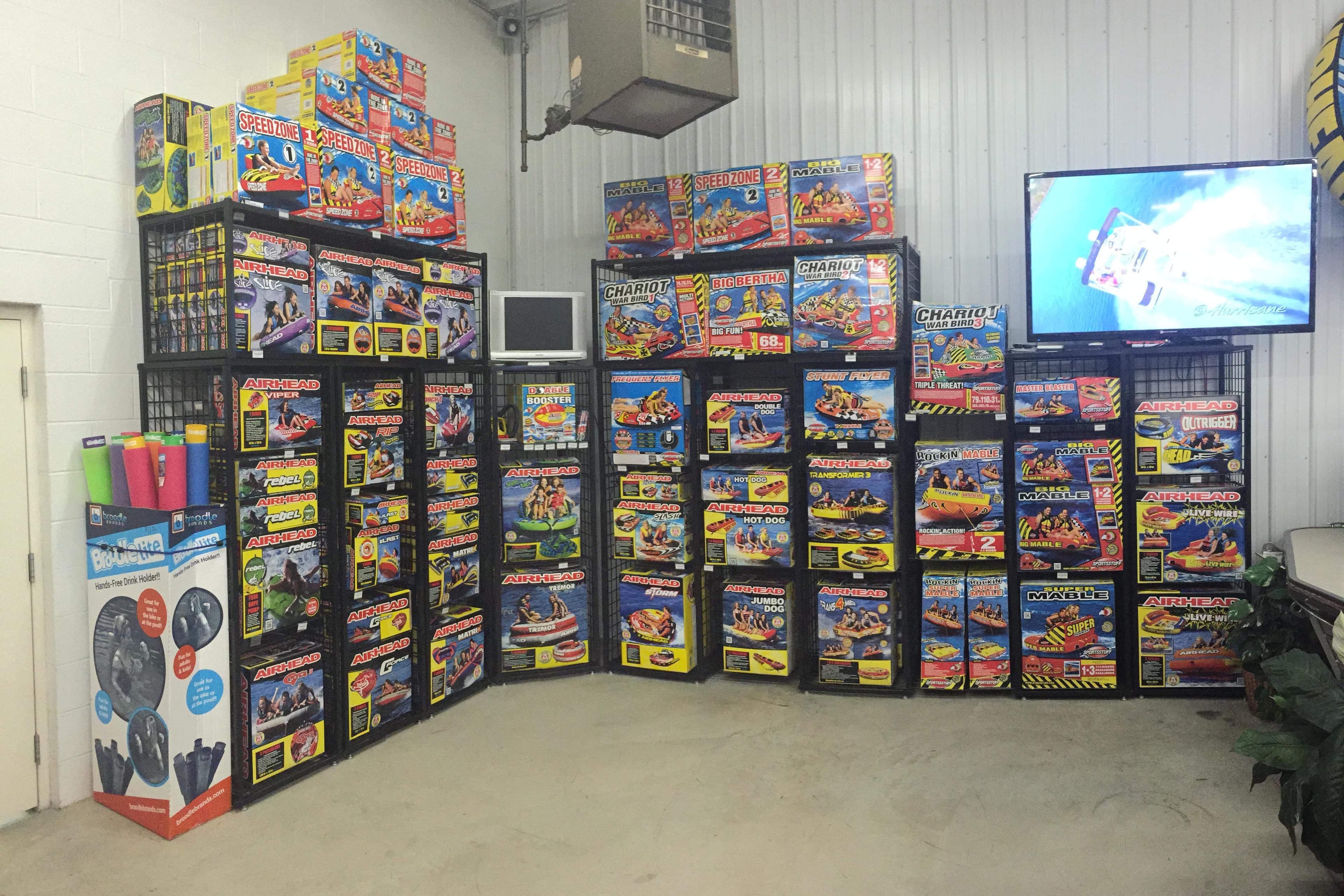 Display of colorful inflatable water sports products in a showroom with a TV screen.