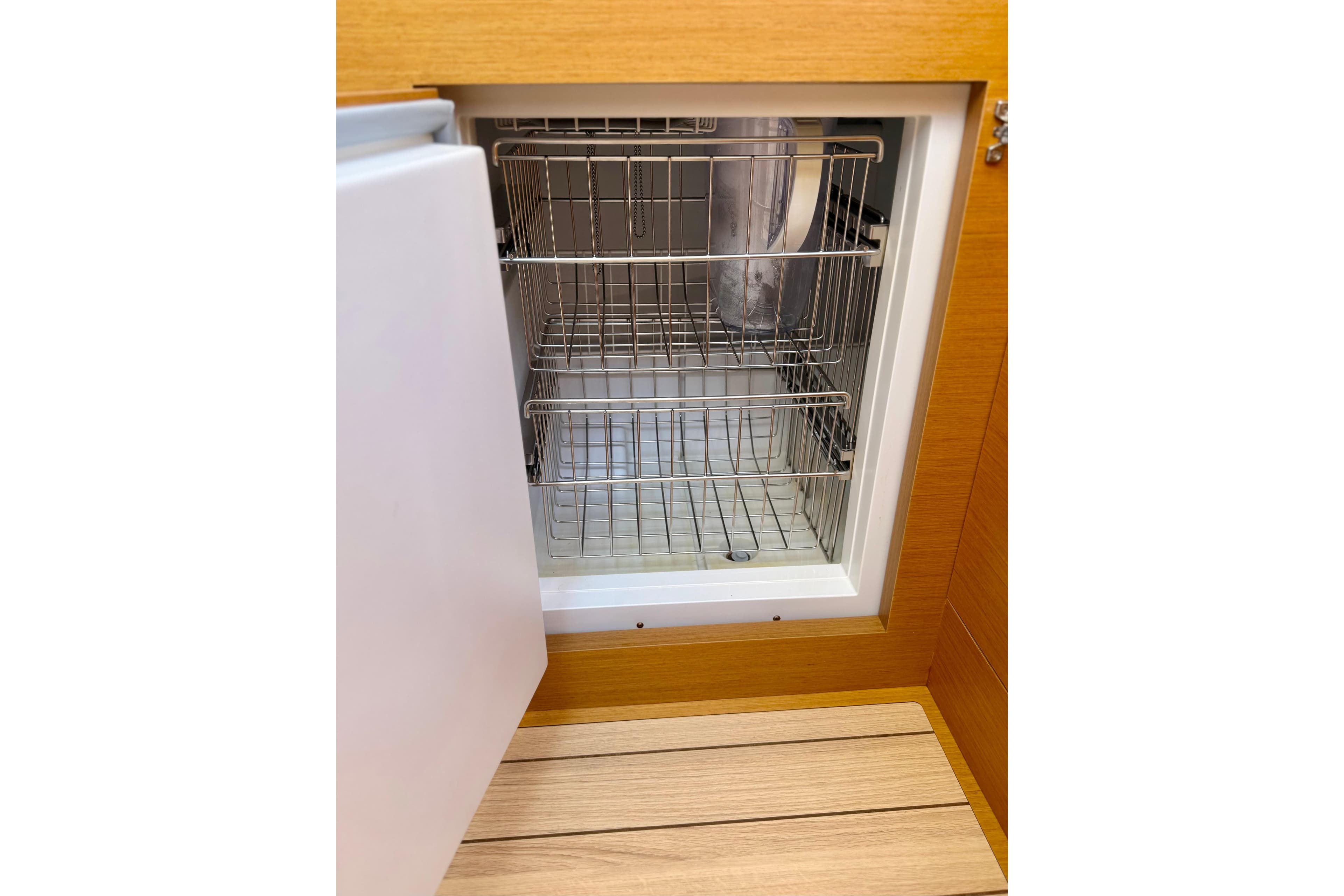 Open refrigerator in 2018 Jeanneau 58 yacht, showcasing wire shelving and wooden flooring.