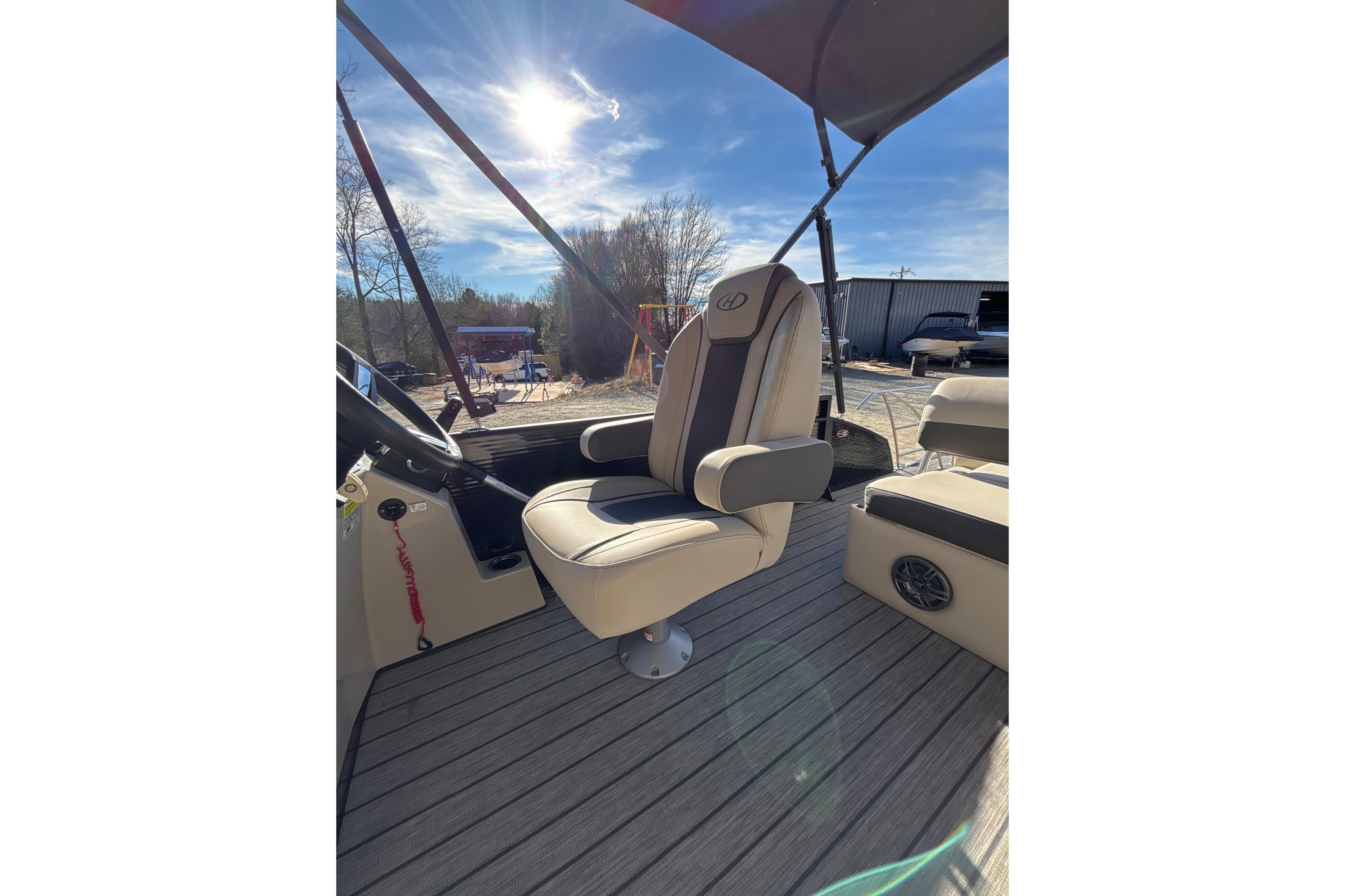 2023 Harris Cruiser 230 boat interior with captain's chair under sunny sky.