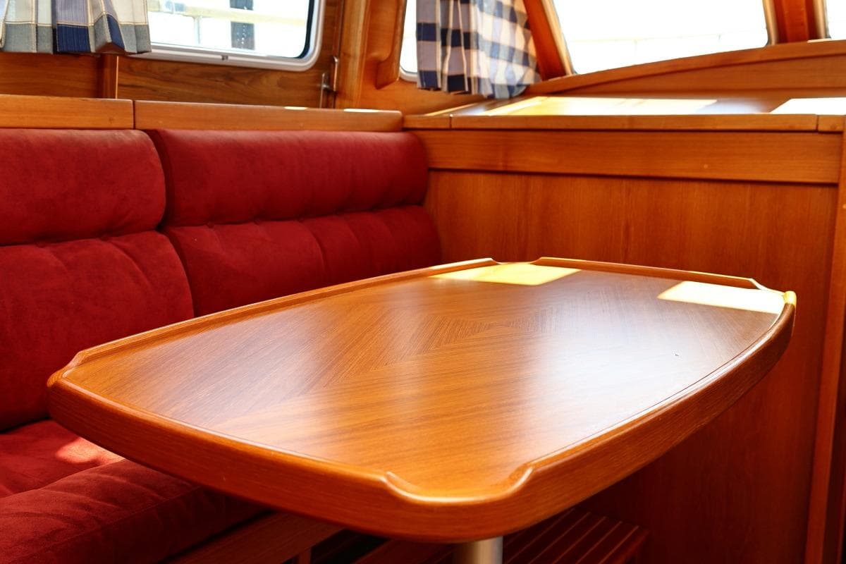 Interior of 2002 Nauticat 331 sailboat with wooden table and red cushioned seating.