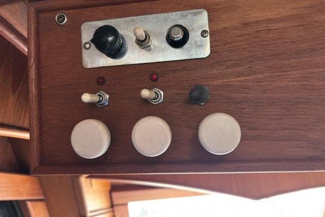 Control panel of a 1983 Canoe Cove Sedan Bridge with switches and knobs on wood.