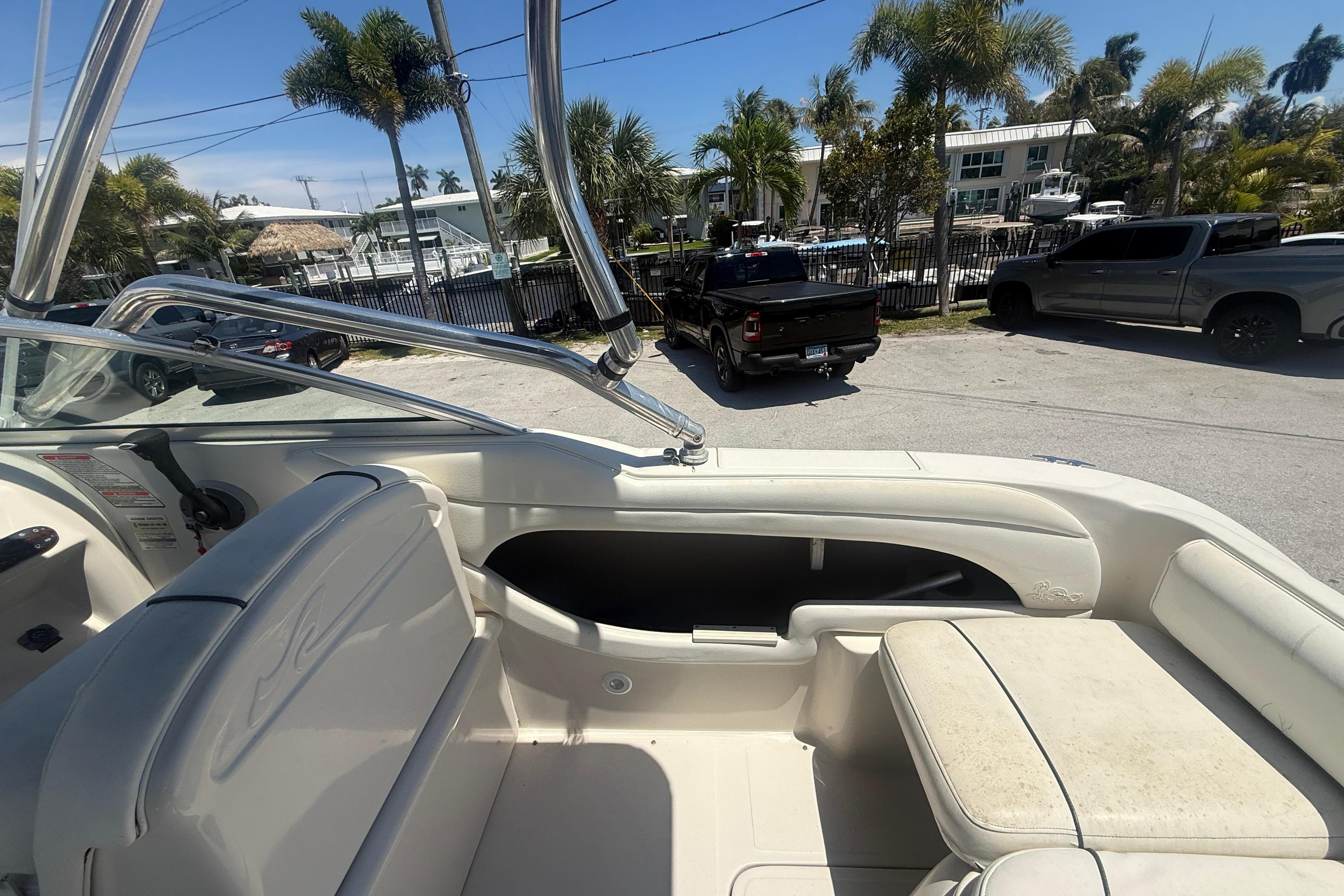 2004 Sea Ray 215 Weekender boat interior with seating, parked near palm trees and vehicles.