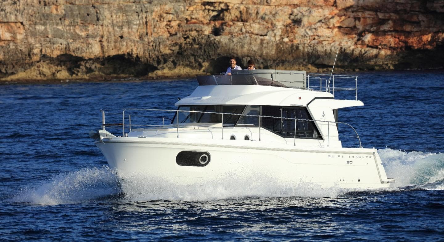 Manufacturer Provided Image: 2020 Beneteau Swift Trawler 30 cruising on blue water near rocky shoreline.