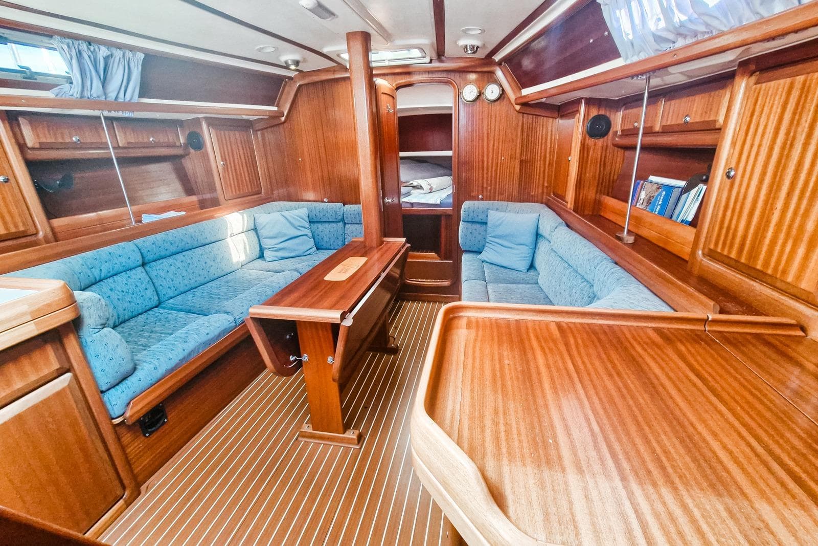 Interior of a 1999 Bavaria 38 Ocean yacht with wooden finish and blue seating.