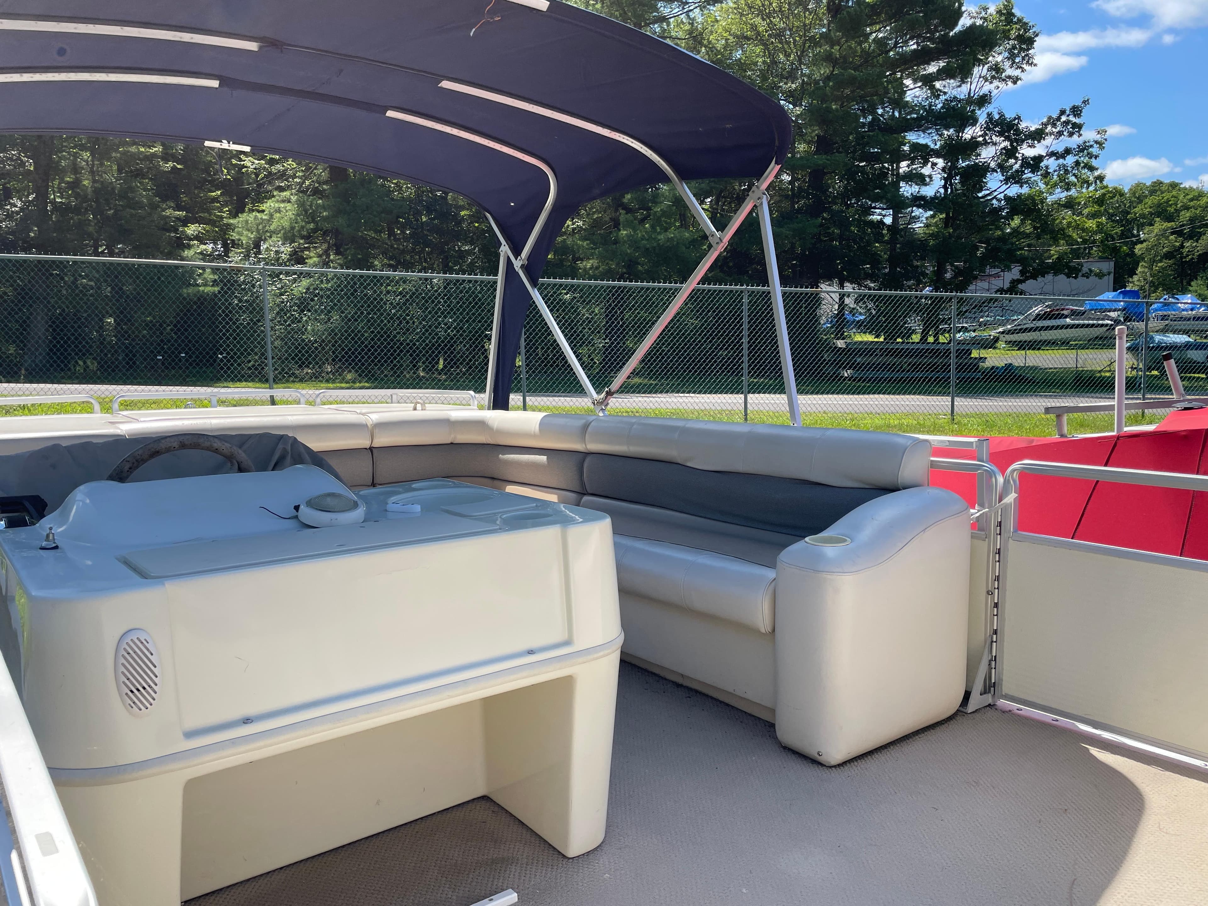 1999 Harris Sunliner 240 pontoon boat interior with seating and canopy, parked outdoors.