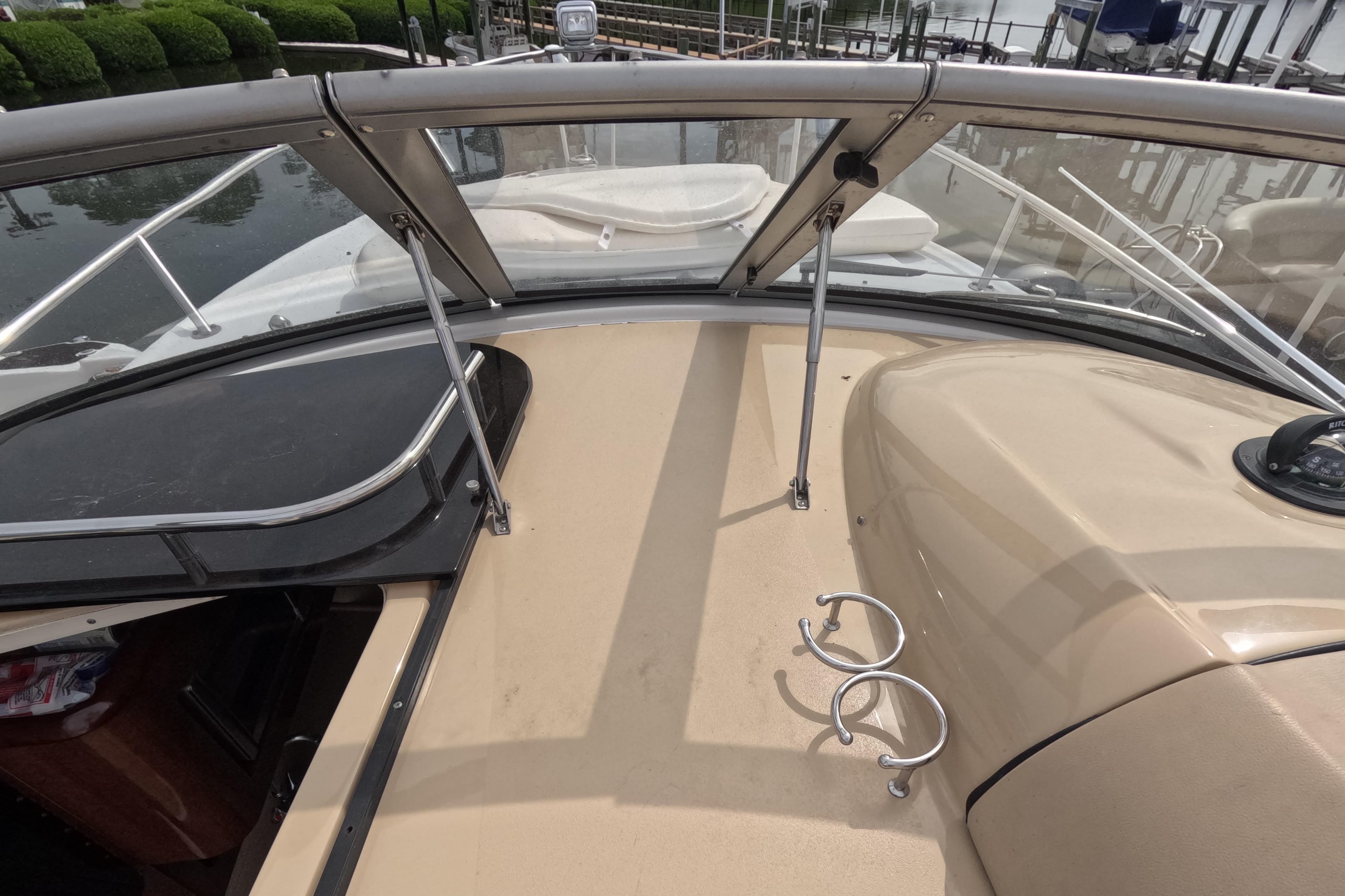 2012 Four Winns V265 boat deck with windshield and cup holders, docked by water.