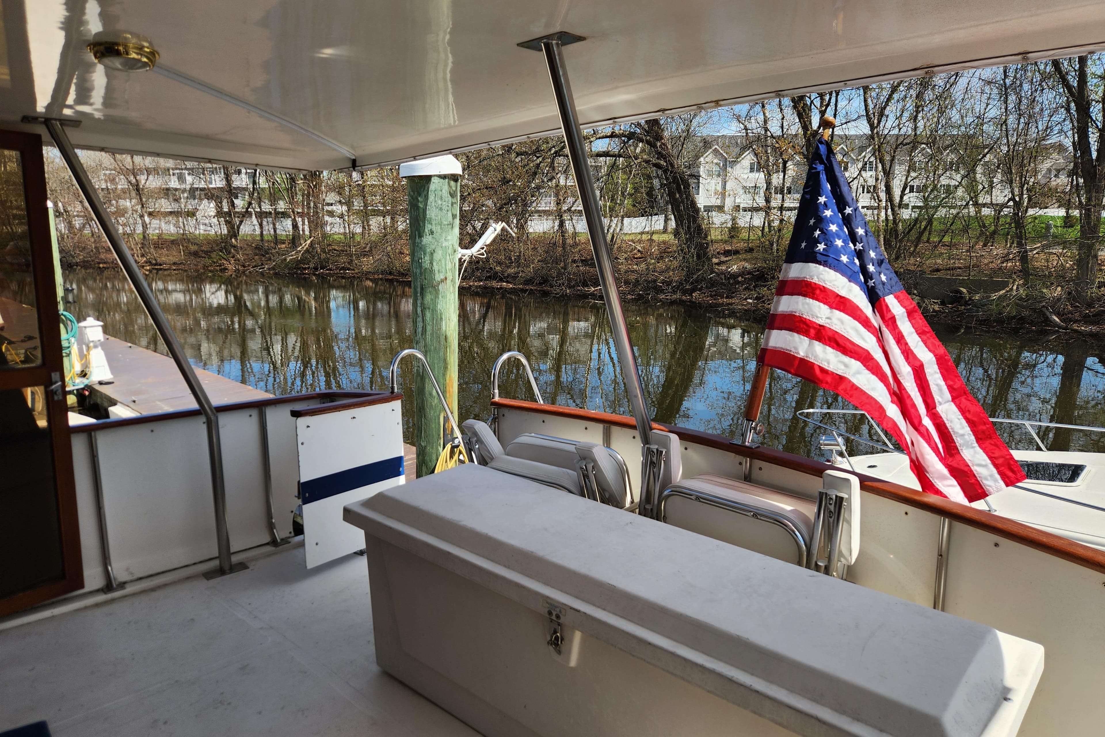 1987 Jefferson 42 SE Sundeck Motor Yacht with American flag, docked by a serene river.
