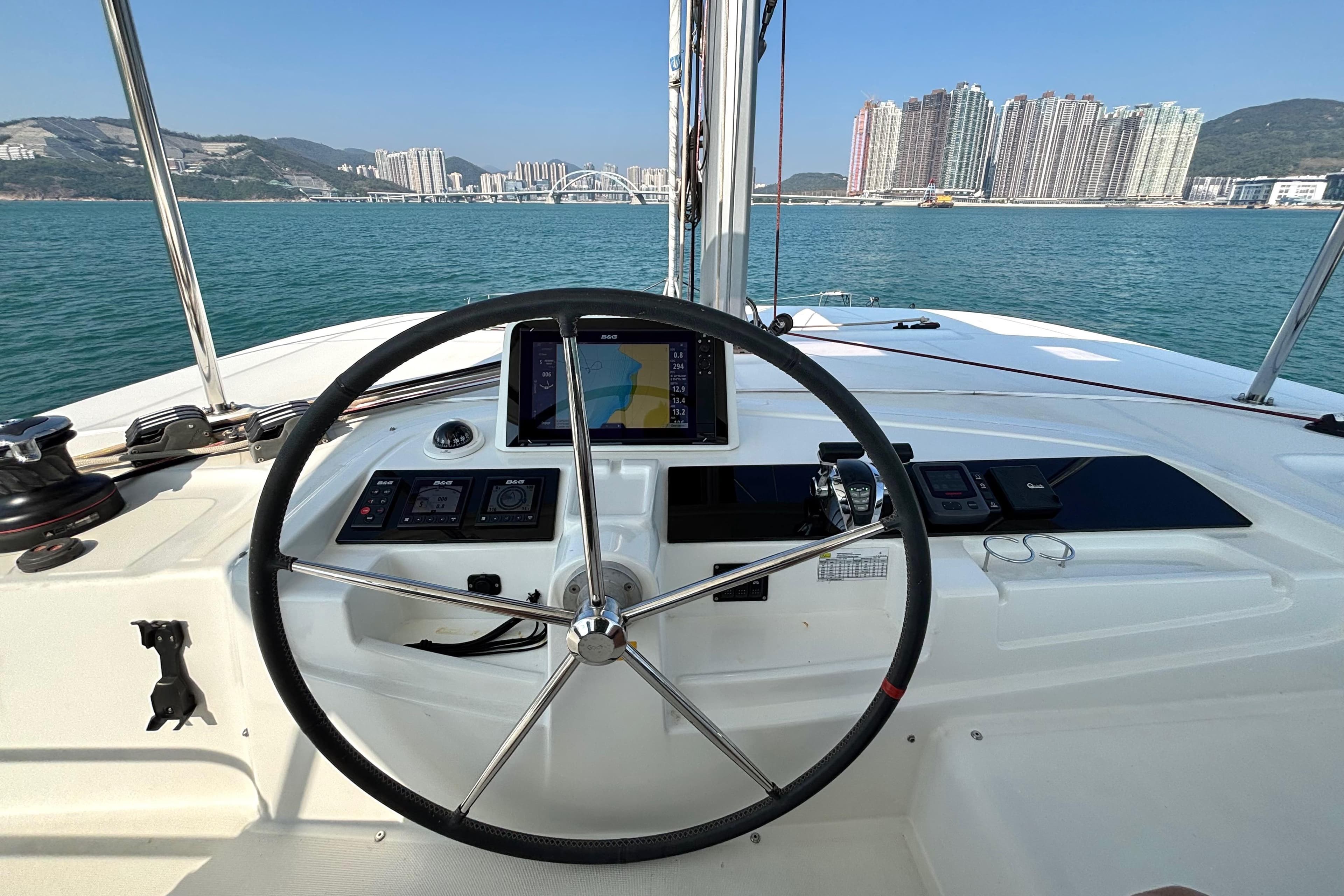 Steering wheel of 2020 Lagoon 46 catamaran with cityscape and ocean view.