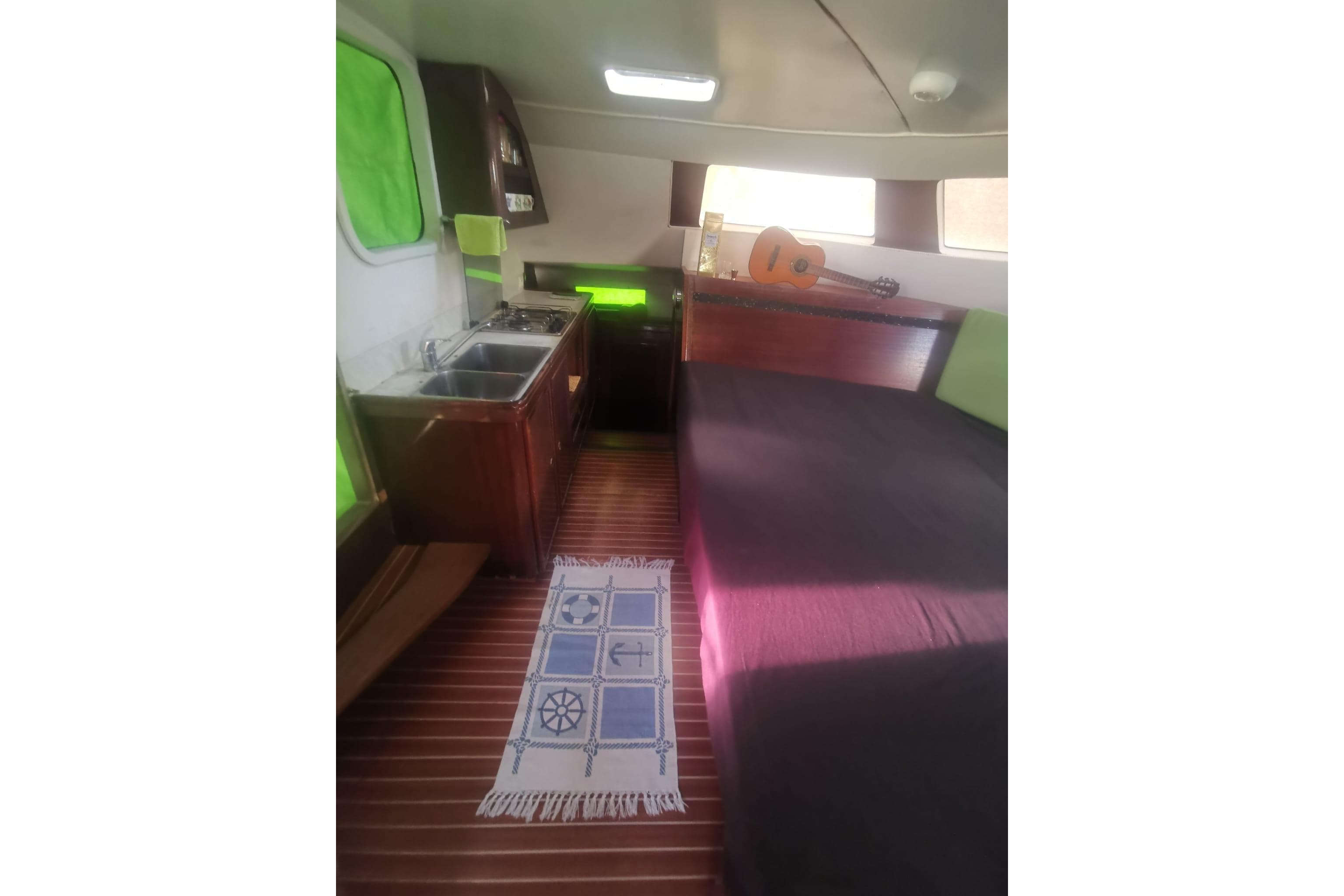 Interior of 1992 Catana 40S yacht with kitchenette, bed, and guitar on wooden floor.