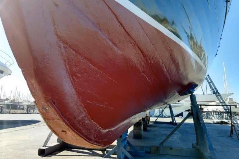 Red hull of a 1940 Brigantin Passagers/Tourisme boat on dry dock.