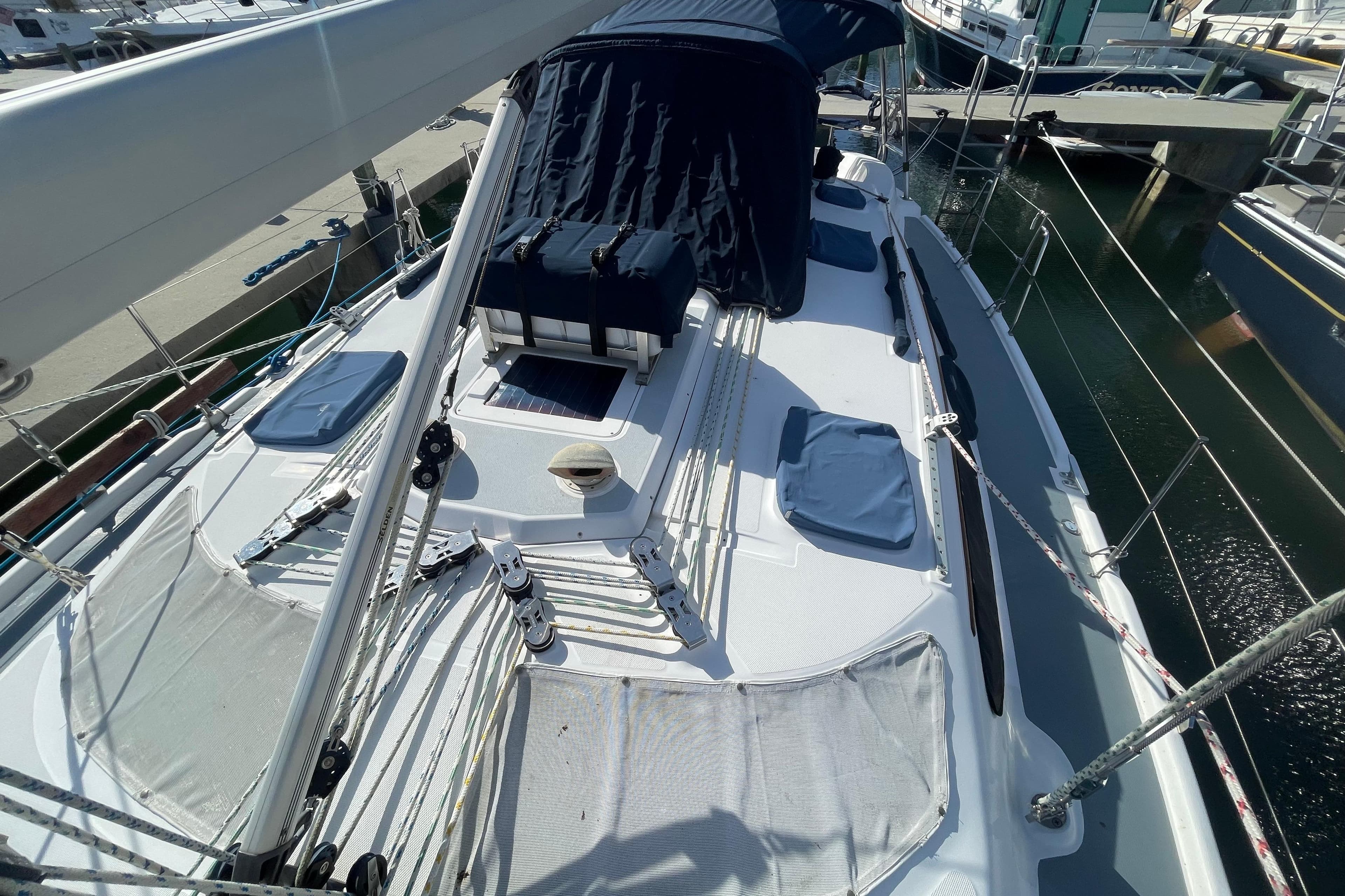 Sailboat deck of 1999 Hunter 460, docked at marina, featuring rigging and blue covers.