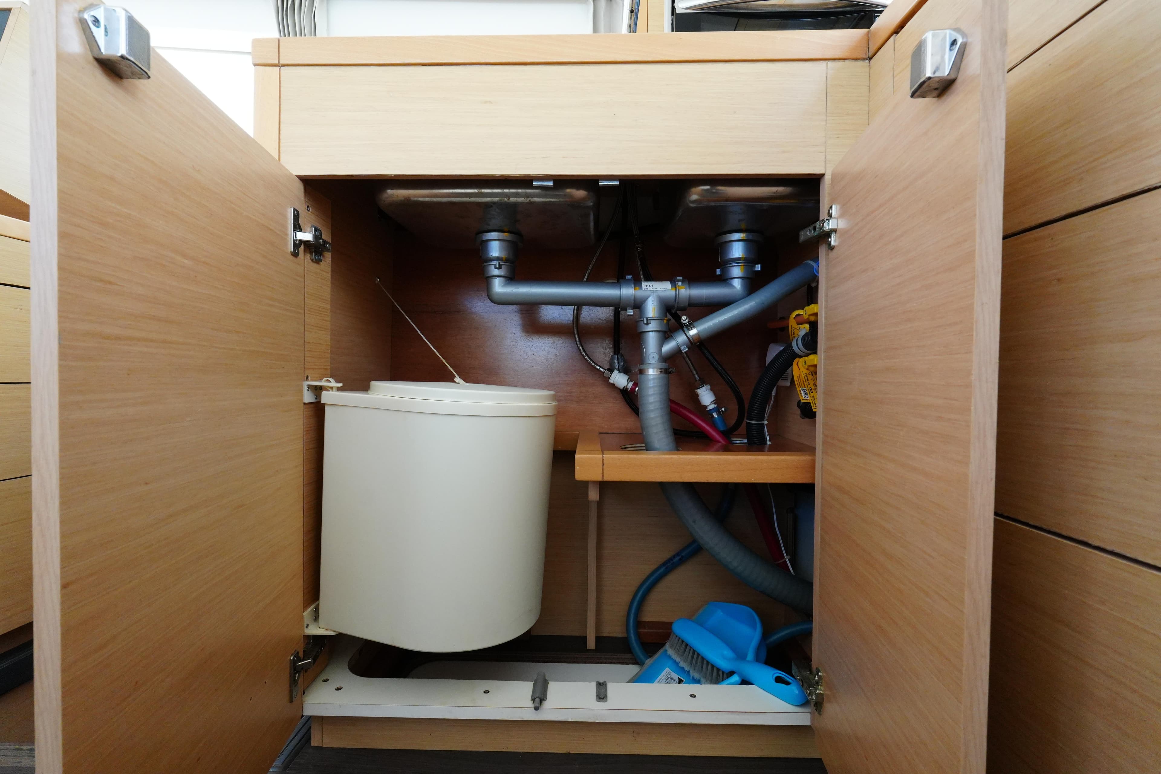 Under-sink storage in 2015 Lagoon 400 S2 yacht, featuring plumbing and cleaning supplies.