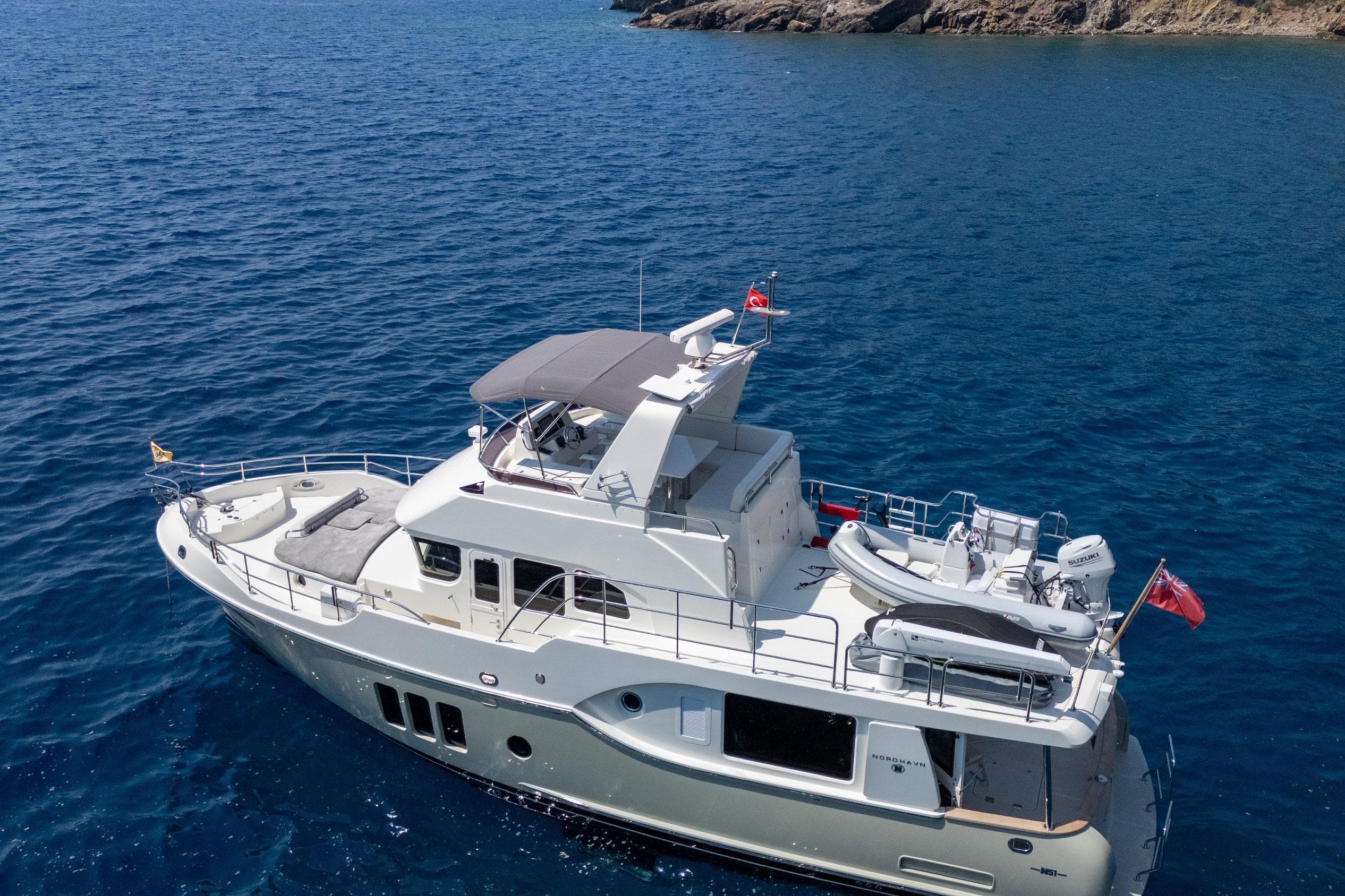 2024 Nordhavn 51 yacht cruising on clear blue waters near rocky coastline.