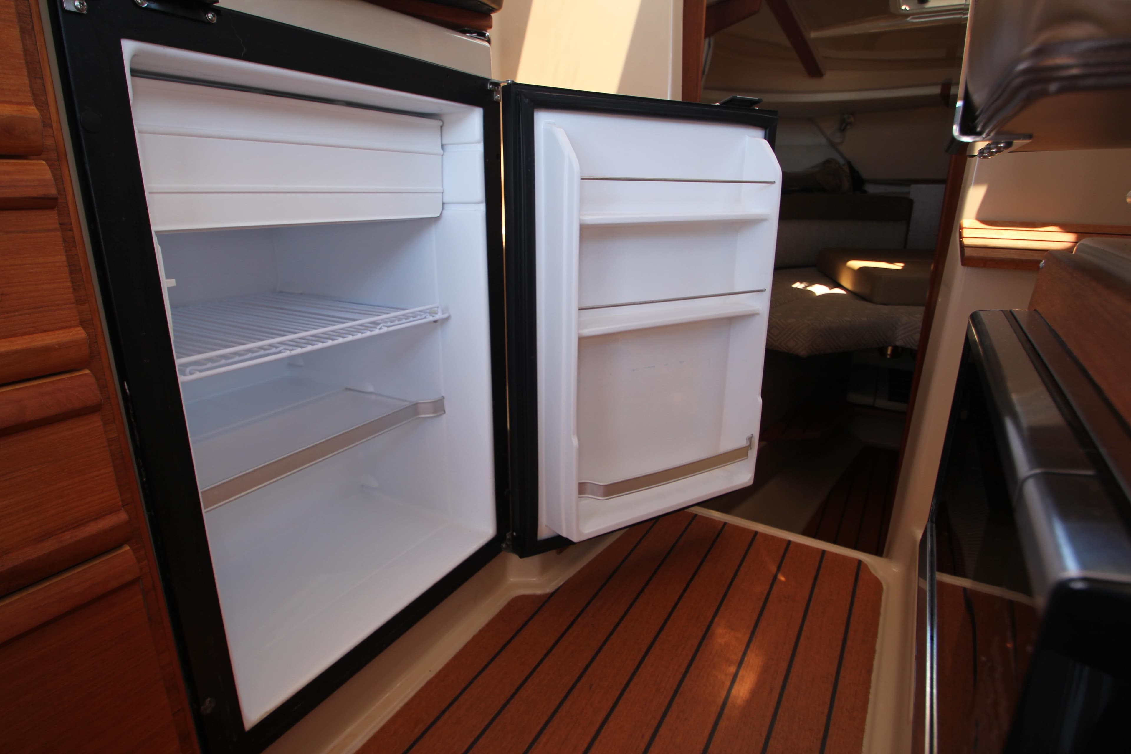 2020 Ranger Tugs R-27 interior with open refrigerator, showcasing wooden flooring and cabin space.