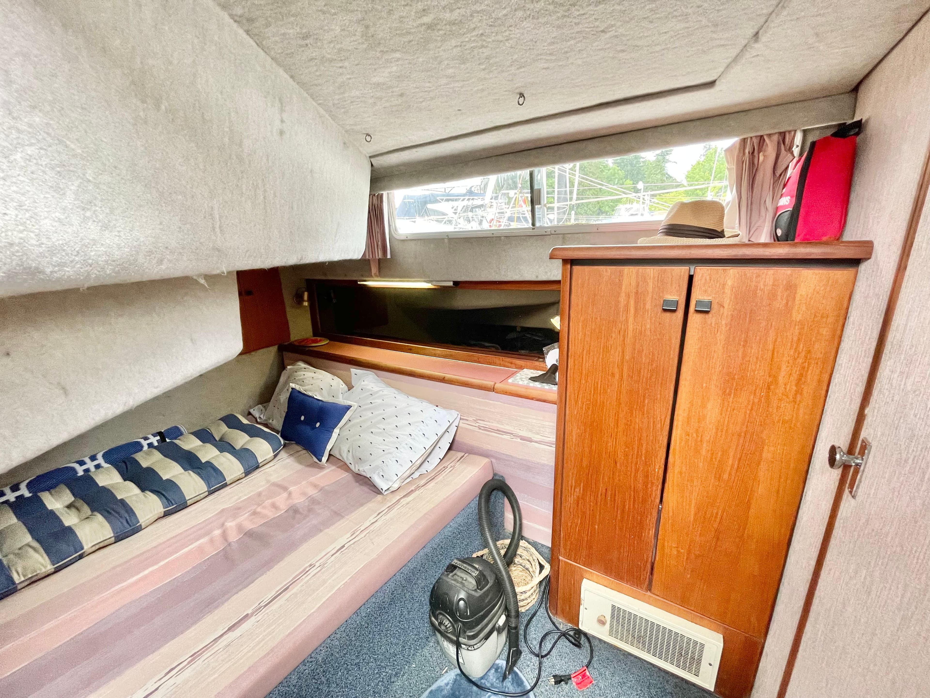 Interior cabin of 1987 Bayliner 3870 Motoryacht with bed, wooden cabinet, and vacuum cleaner.