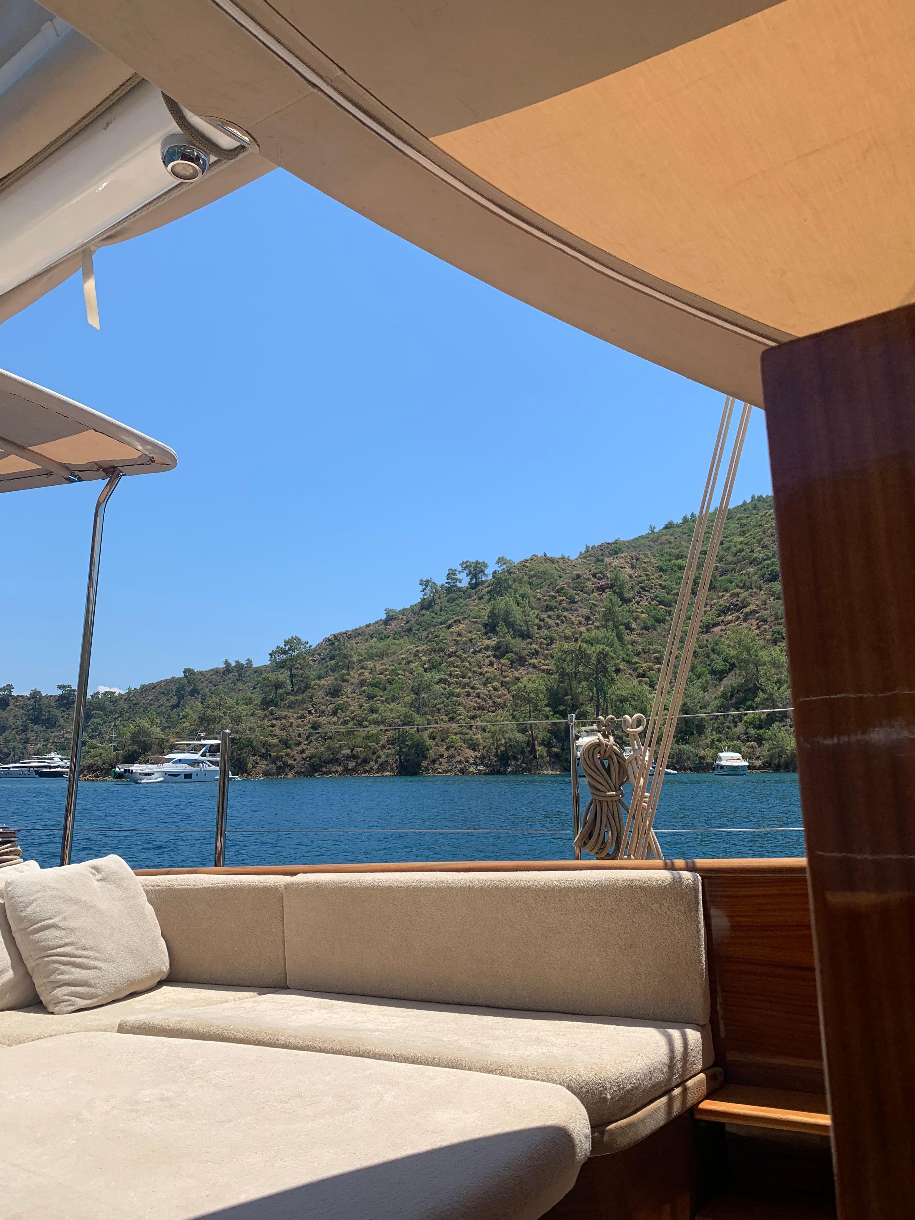 Luxury yacht deck with sunbed, overlooking serene blue waters and lush green hills.