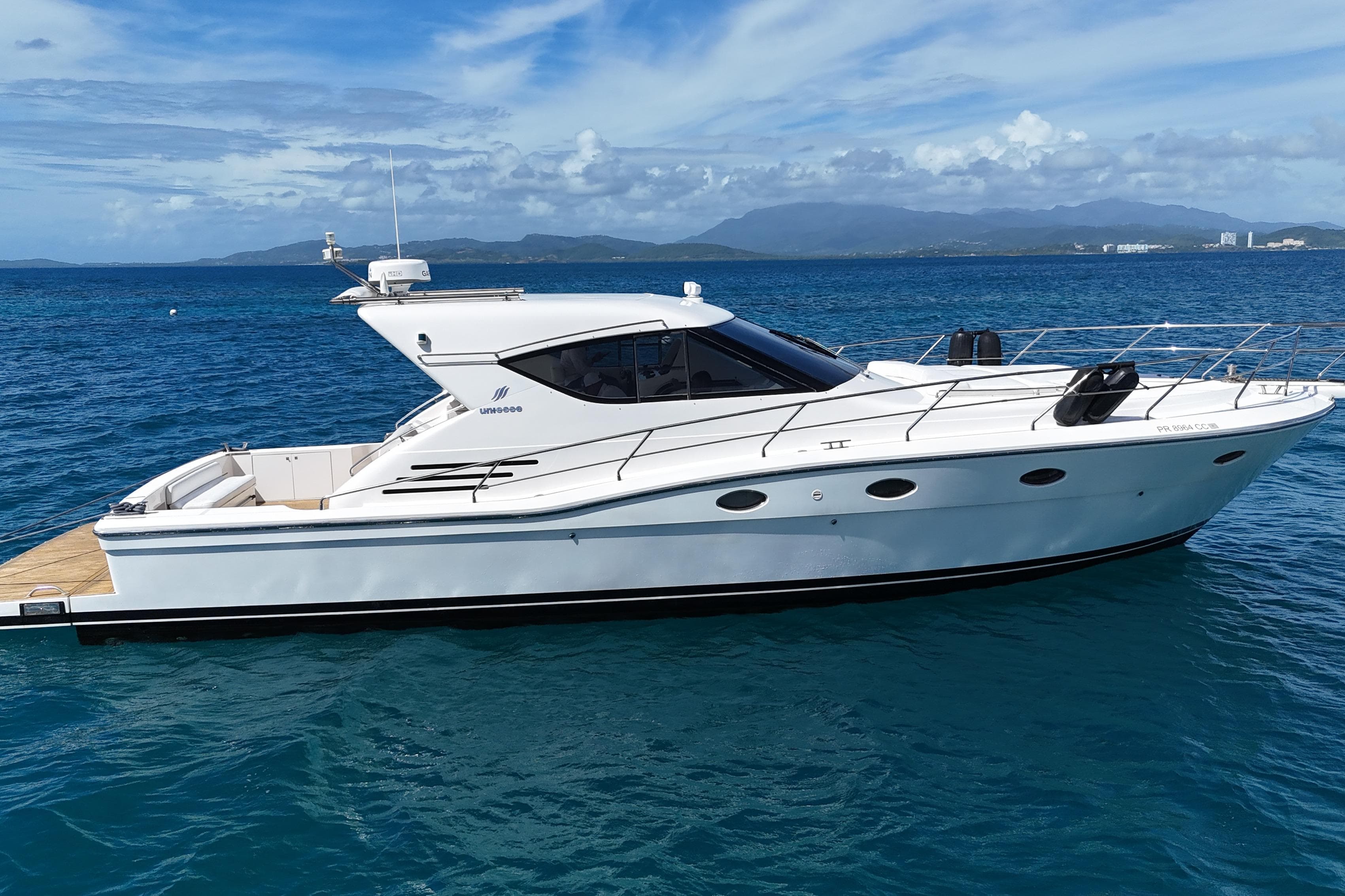 2013 Uniesse 49 yacht on clear blue water with scenic mountain backdrop.