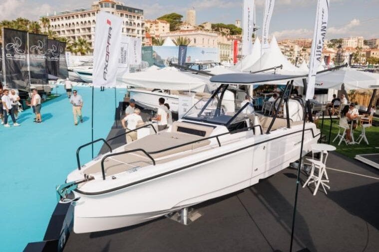 2027 Axopar 25 Cross Top boat displayed at a marina event with people and banners.