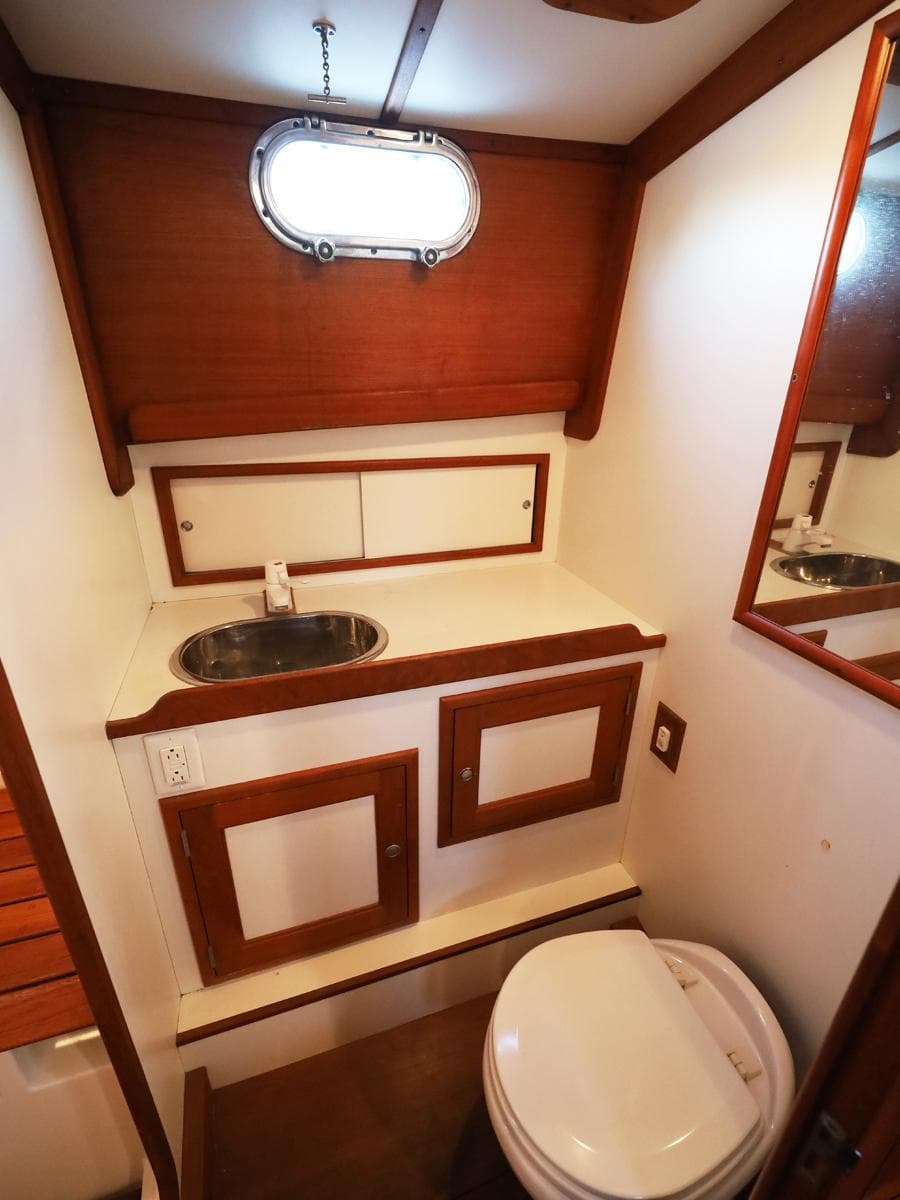 Wood-accented boat bathroom with sink, mirror, and porthole window, Able 44, 1995 model.