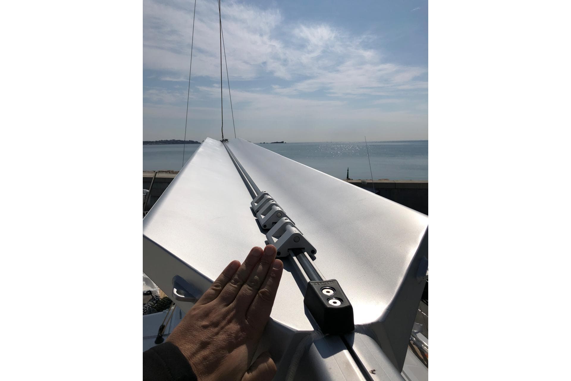 Hand on Jeanneau 54 sailboat mast, 2018 model, with ocean view in background.