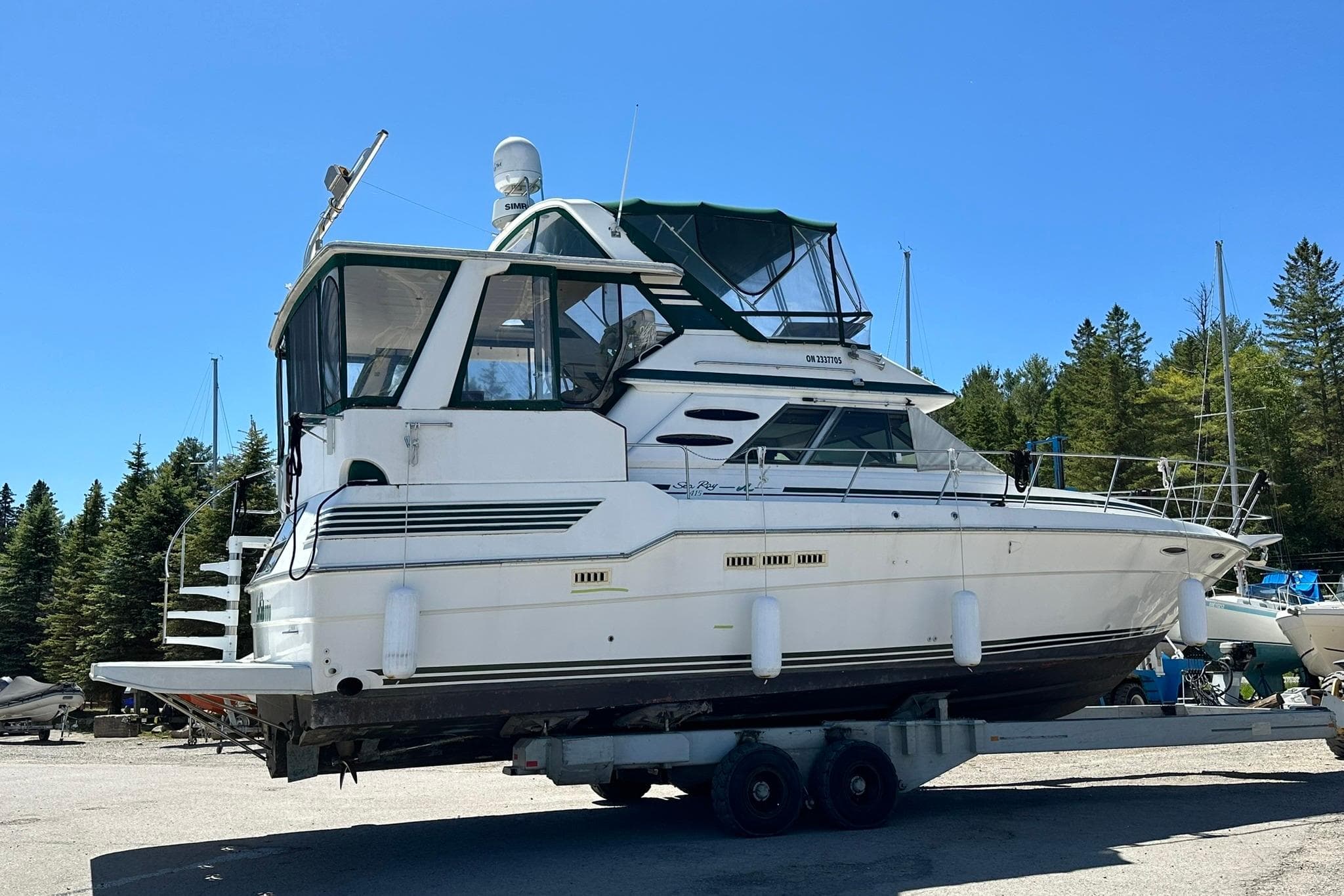 1988 Sea Ray 415 Aft Cabin yacht on trailer, surrounded by trees and clear blue sky.