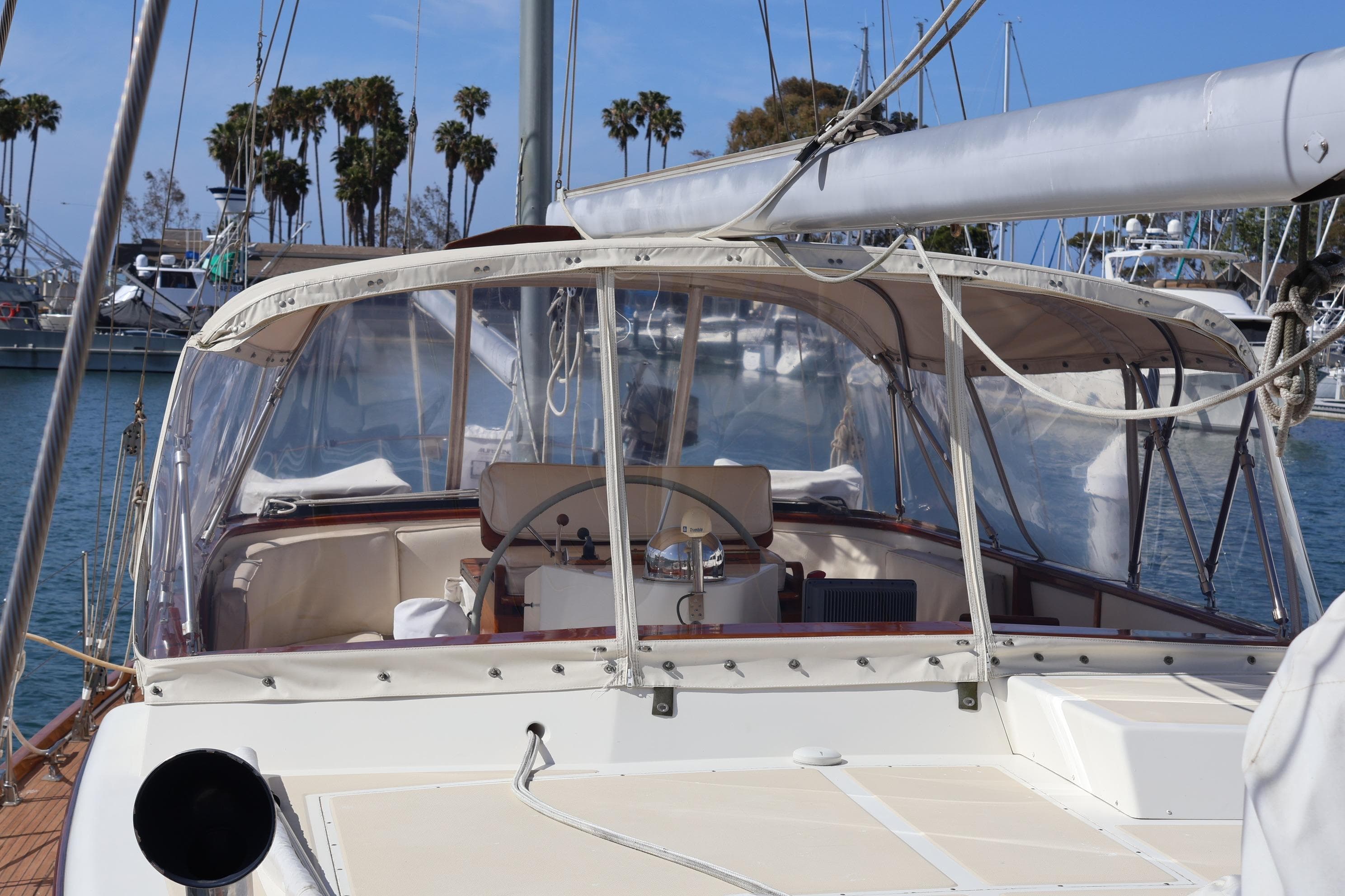 1984 Mason 63 sailboat cockpit with clear canopy, docked in a marina with palm trees.