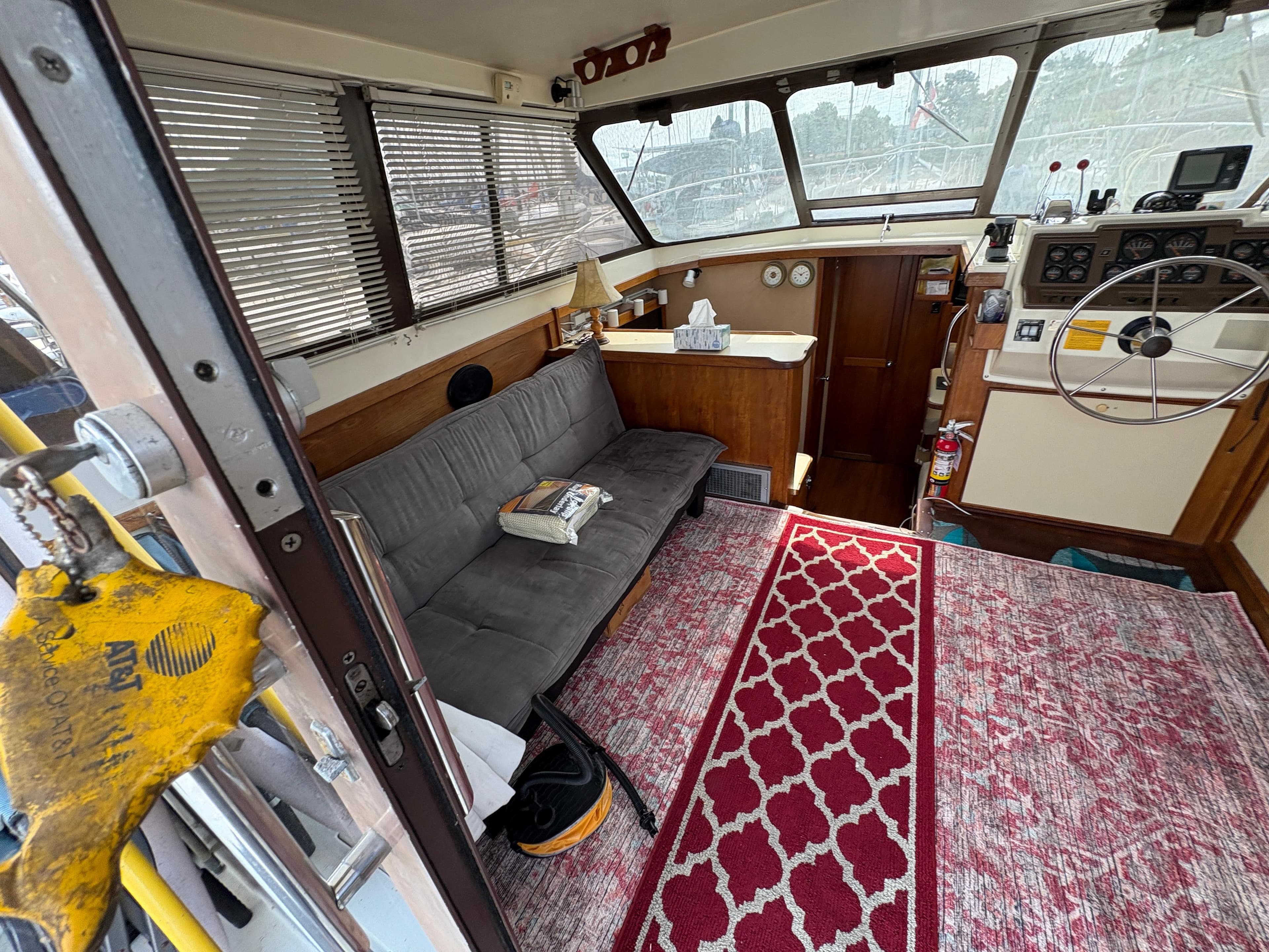 Interior of a 1986 Trojan 32 Sedan boat with sofa, steering wheel, and red patterned rug.
