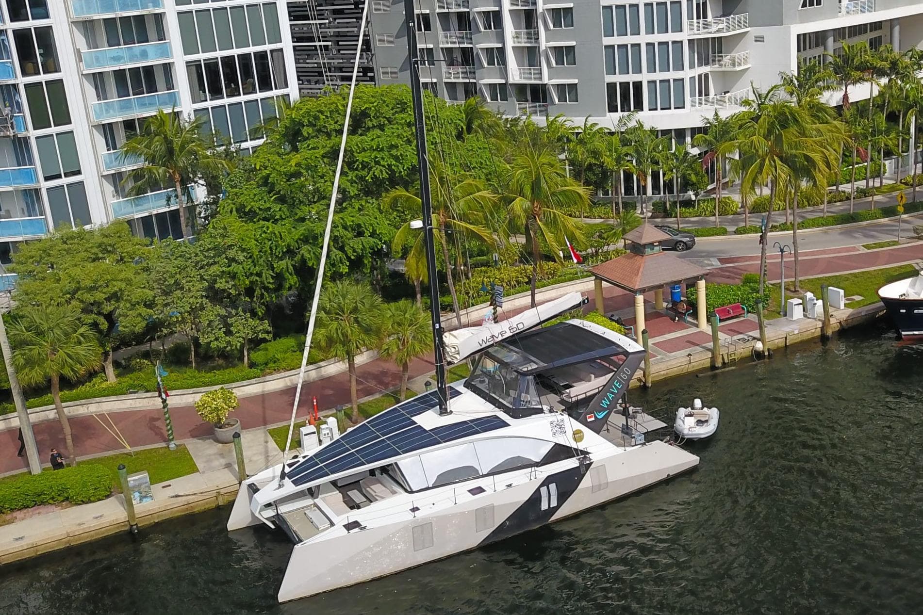 2024 Wave Wave60 catamaran docked near modern waterfront buildings and lush greenery.