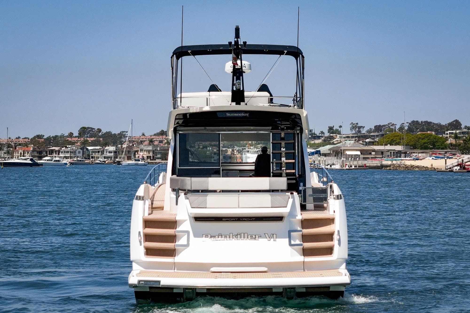 2023 Sunseeker 65 Sport Yacht on water, rear view, coastal background.