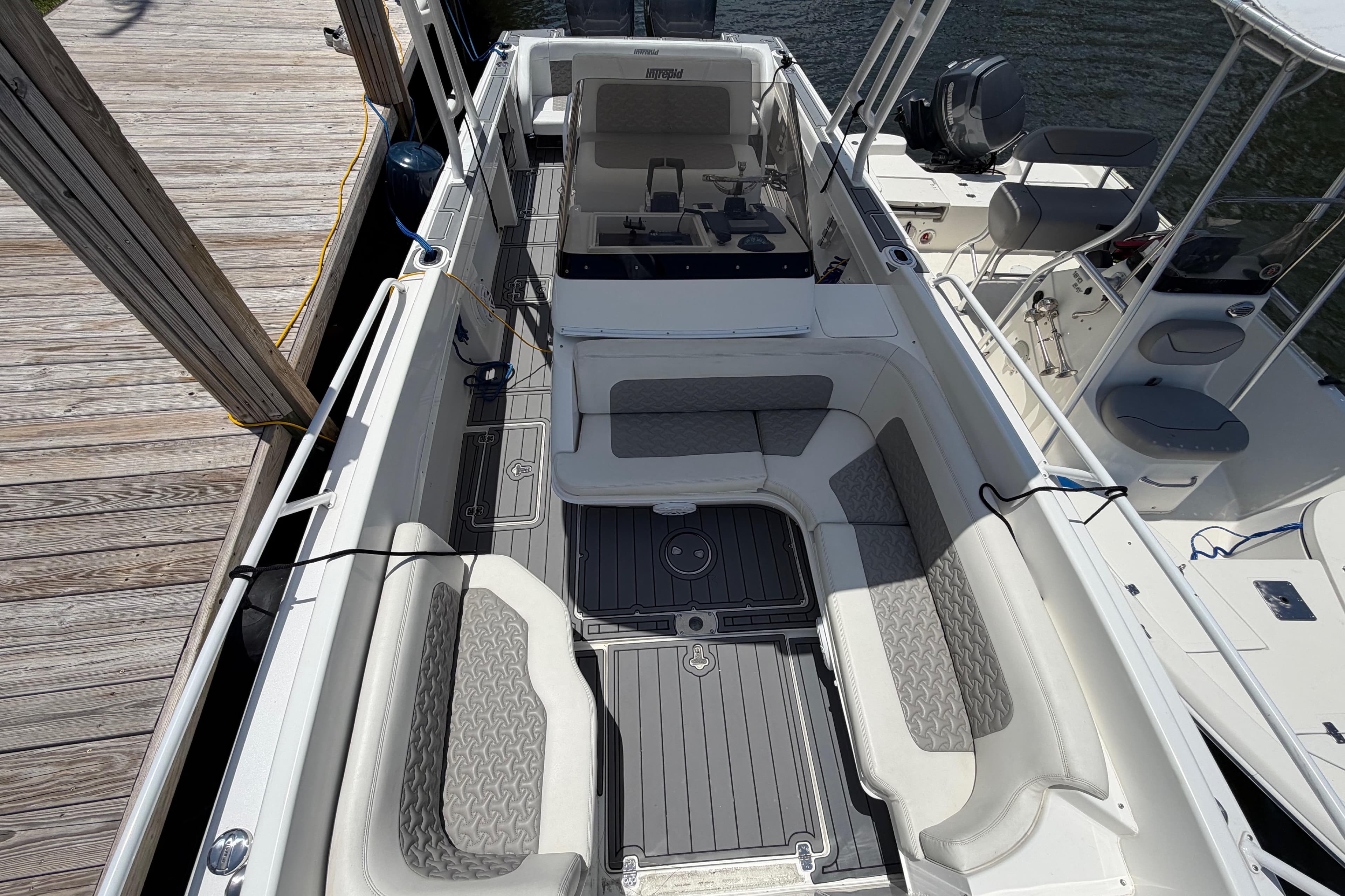 2003 Intrepid 323 Cuddy boat interior with cushioned seating and deck, docked by wooden pier.